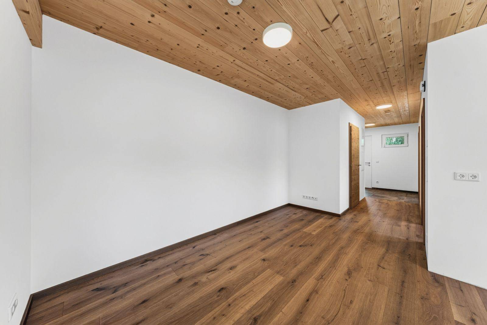 Langer Flur mit Holzboden, Holzdecke und weißen Wänden, der zu weiteren Räumen führt.