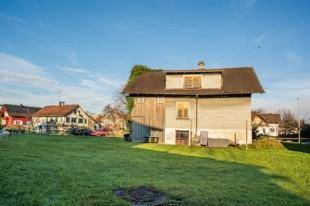 Seitenansicht des Gebäudes mit Holzfassade und Dachgaube, umgeben von grünem Rasen.