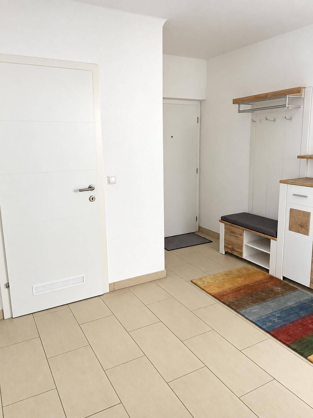 Heller Eingangsbereich mit Fliesenboden und moderner Garderobe, die viel Stauraum bietet.