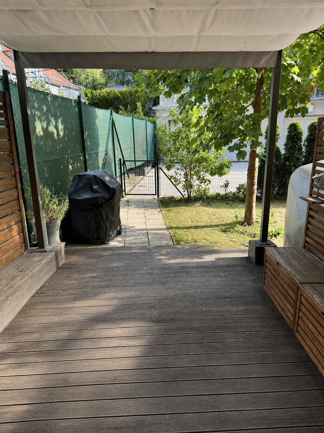 Überdachte Terrasse mit Holzboden und Blick auf den Garten, ideal für Grillabende im Freien.