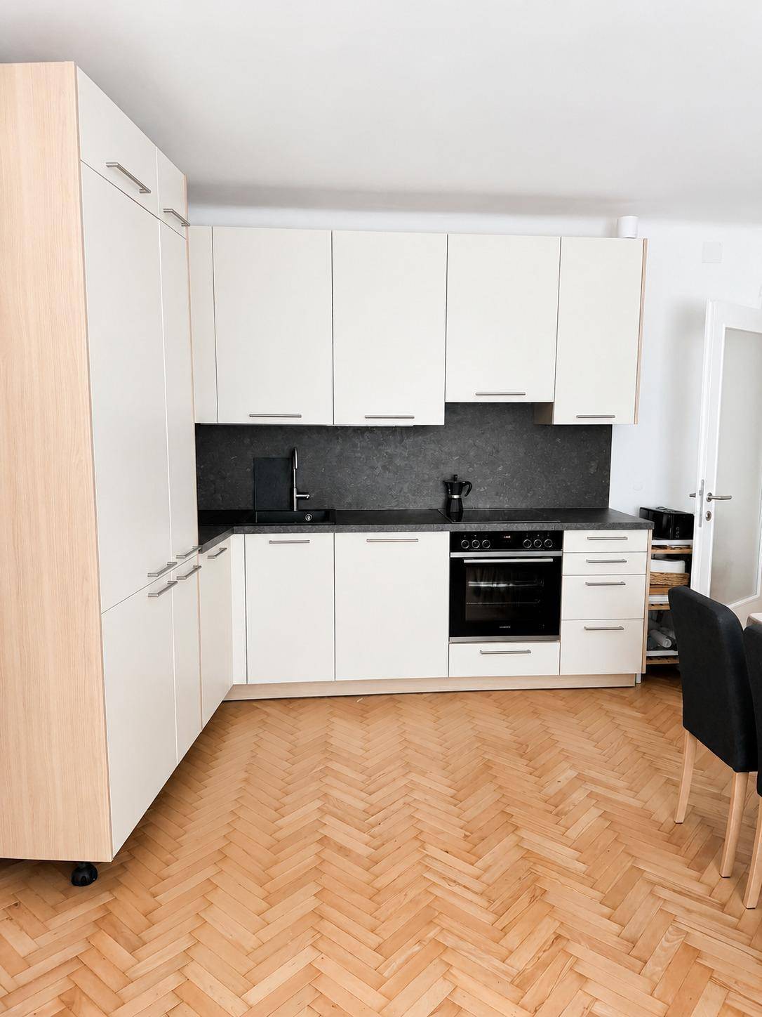 Moderne Einbauküche mit hellen Fronten, dunkler Arbeitsplatte und Fischgrätparkettboden.