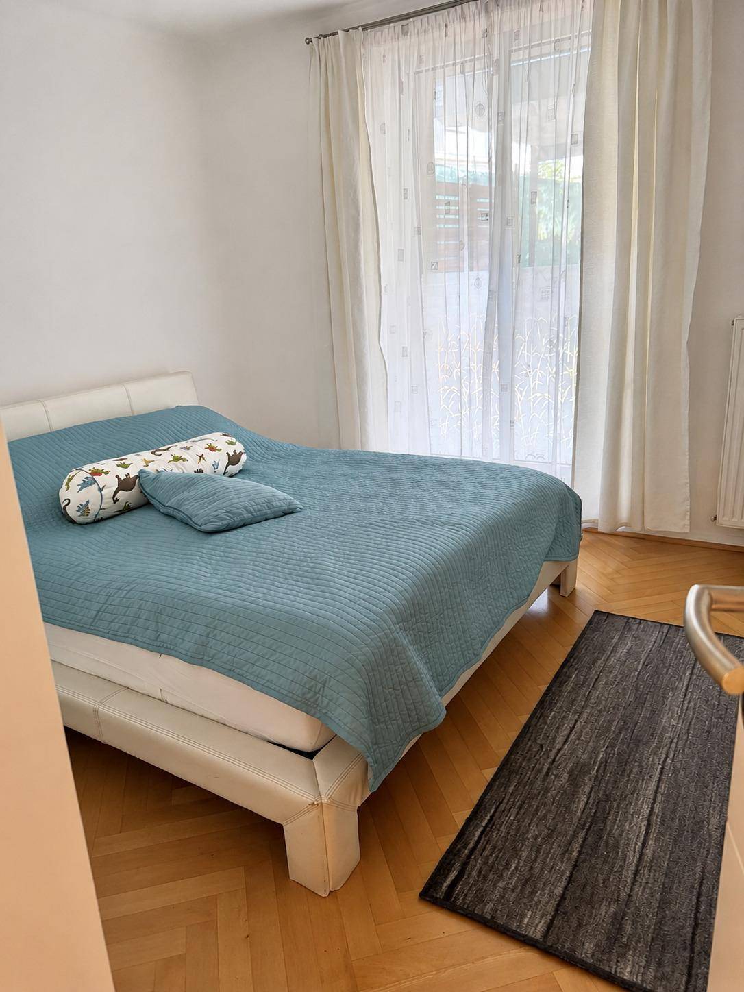 Gemütliches Schlafzimmer mit Doppelbett, Parkettboden und hellem Fenster für viel Tageslicht.