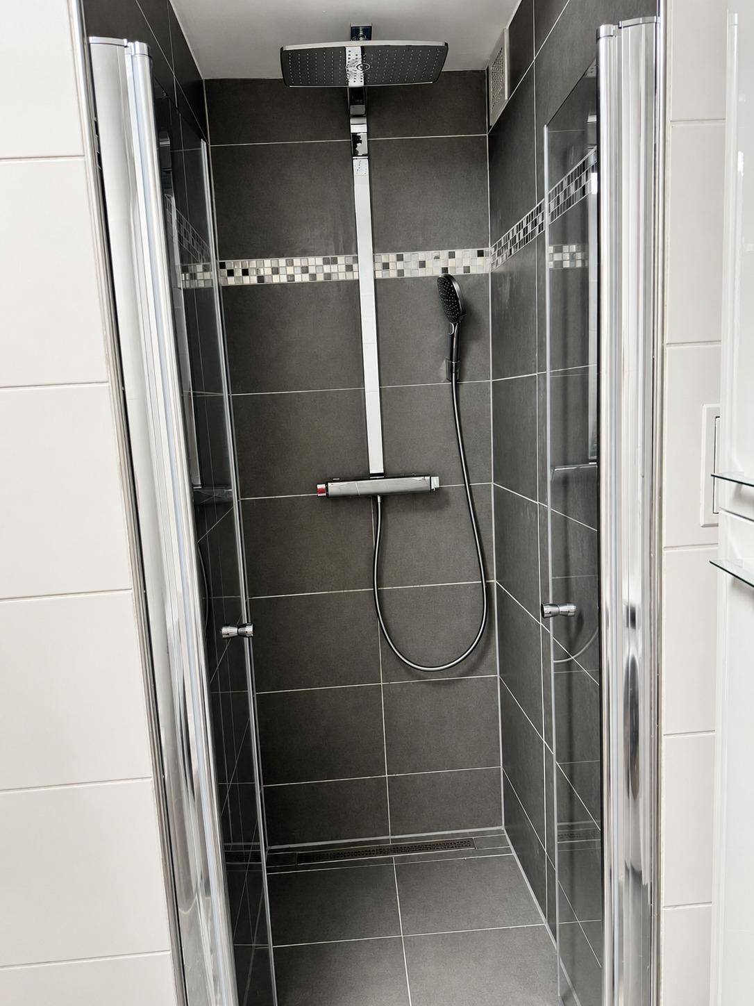 Moderne Duschkabine mit dunklen Fliesen, Regendusche und Glasabtrennung im Badezimmer.