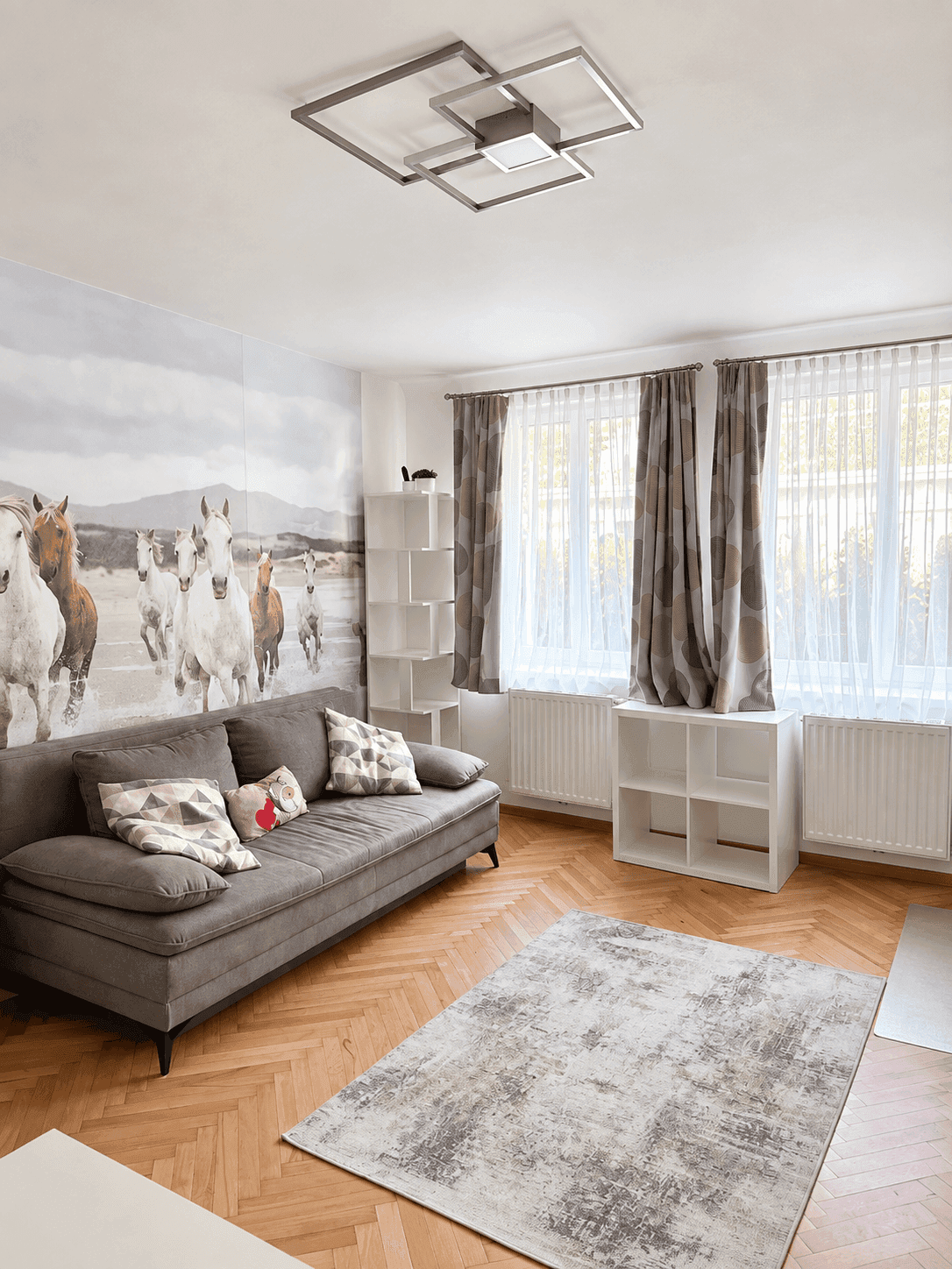 Geräumiges Wohnzimmer mit Parkettboden, großer Fensterfront und einer auffälligen Pferdetapete.