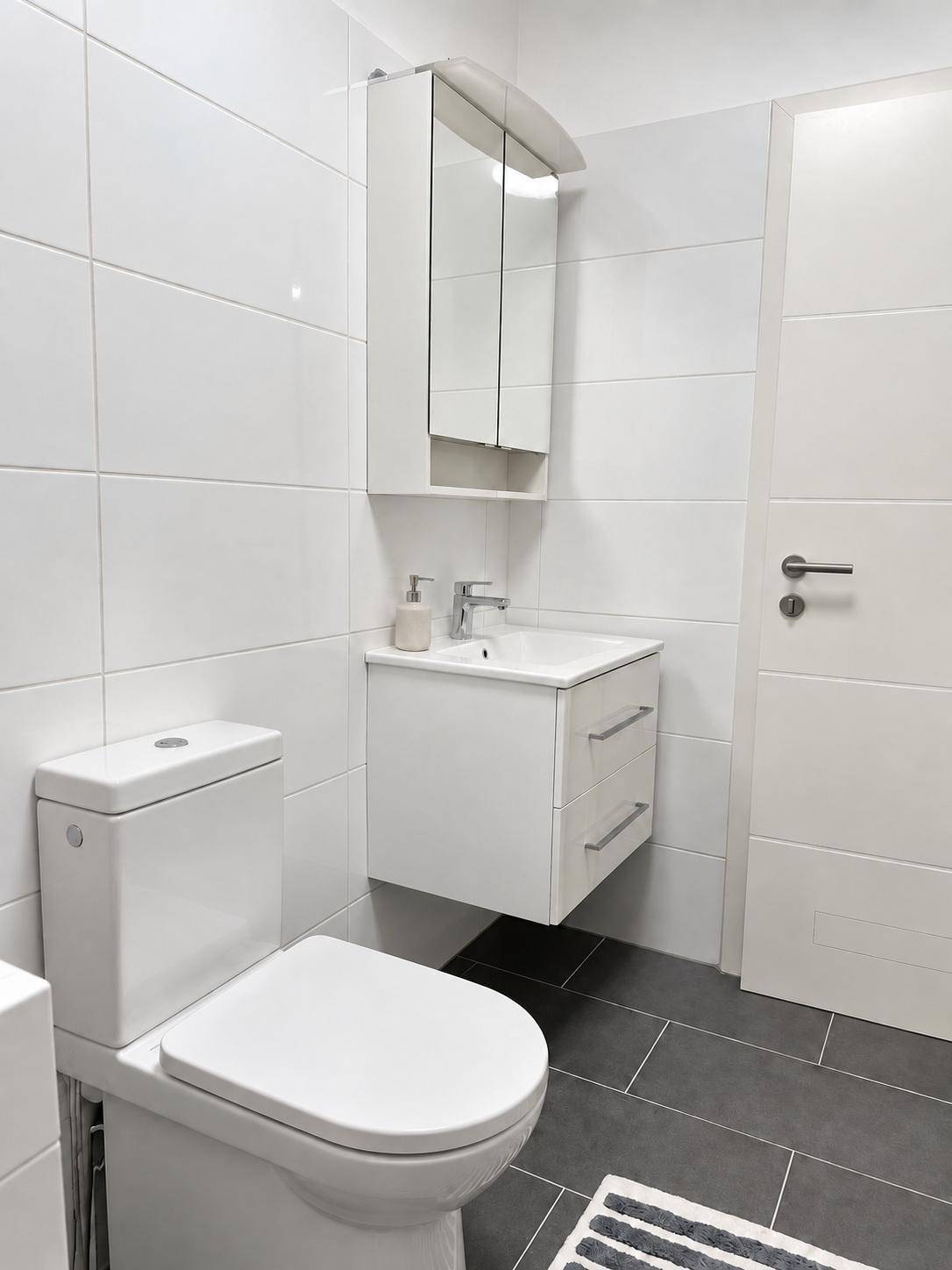 Modernes Badezimmer mit dunklen Bodenfliesen, weißer Wandverkleidung und schwebendem Waschtisch.