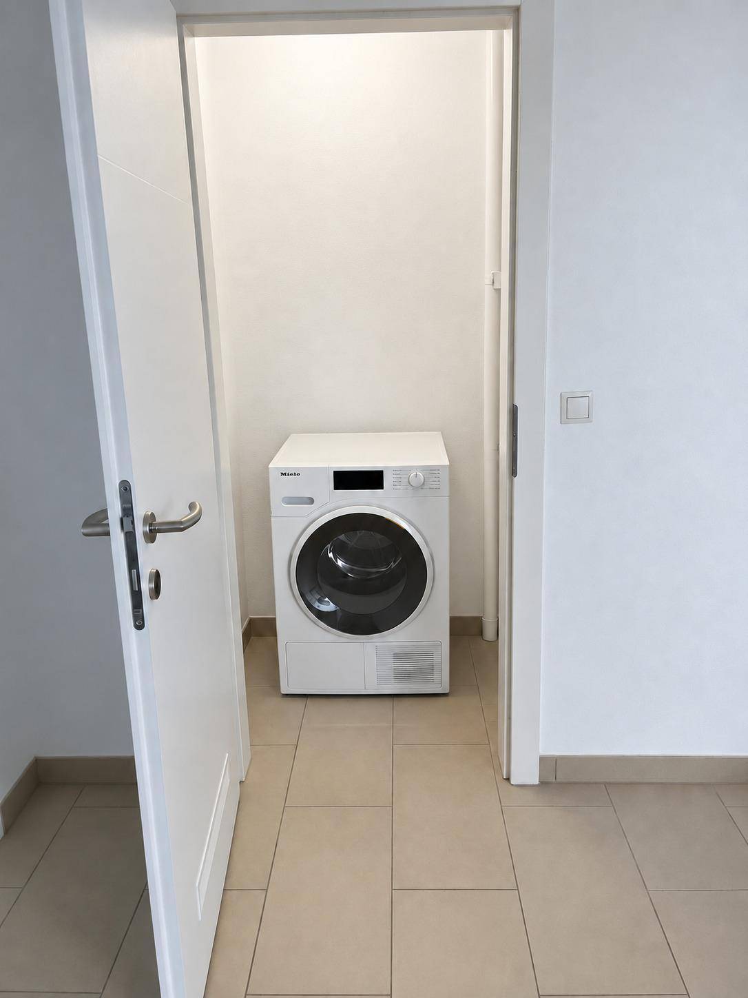 Praktischer Hauswirtschaftsraum mit Trockner und hellem Fliesenboden, ideal für die Wäschepflege.
