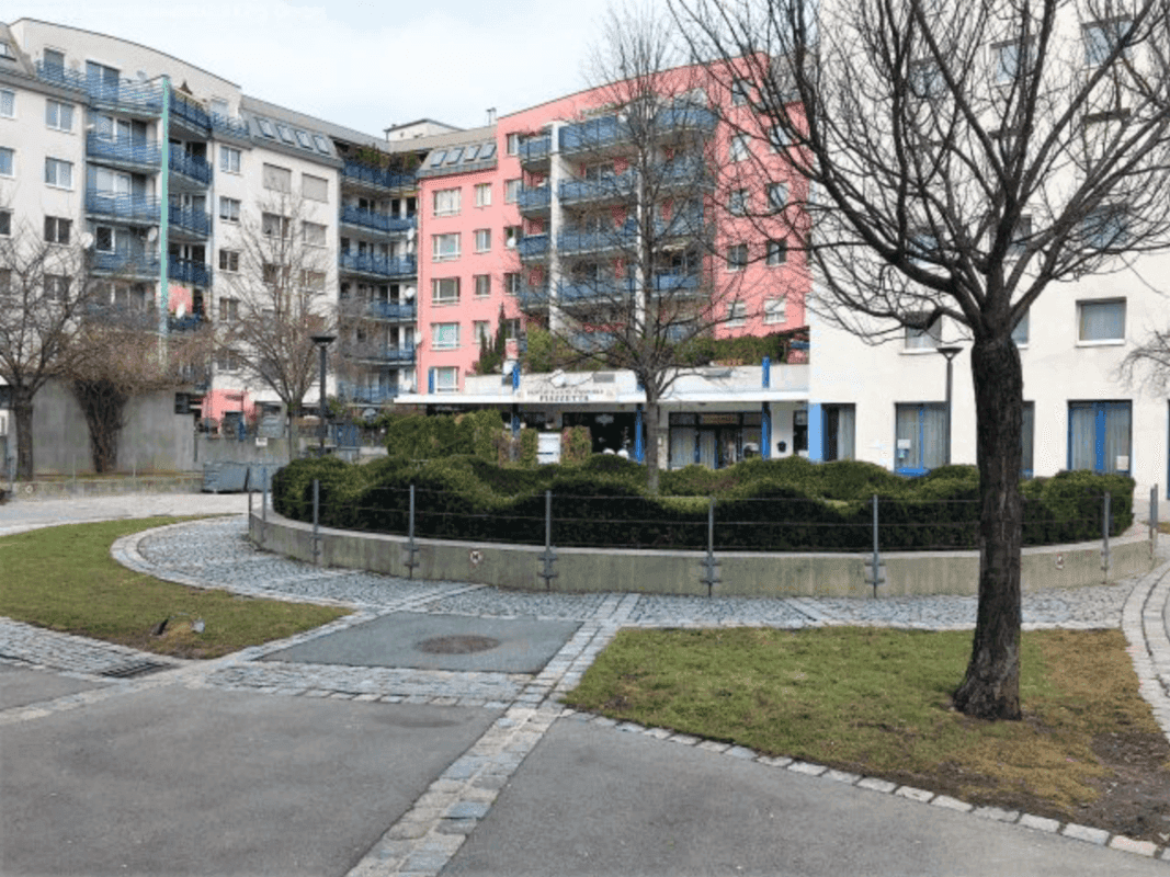 Wohnkomplex mit begrüntem Innenhof und Bäumen, umgeben von modernen Gebäuden in städtischer Umgebung.