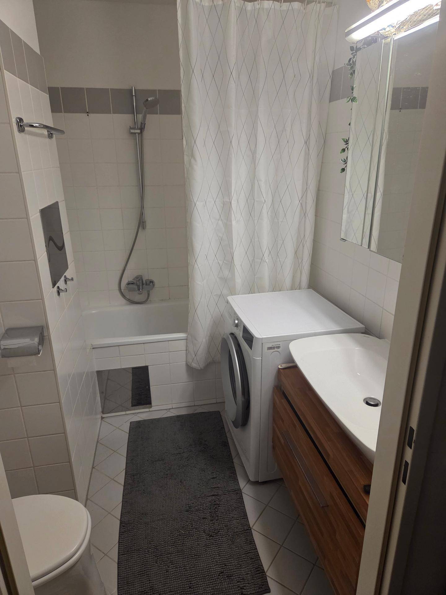 Funktionales Badezimmer mit Badewanne, Waschmaschine und modernem Waschtisch für den täglichen Gebrauch.