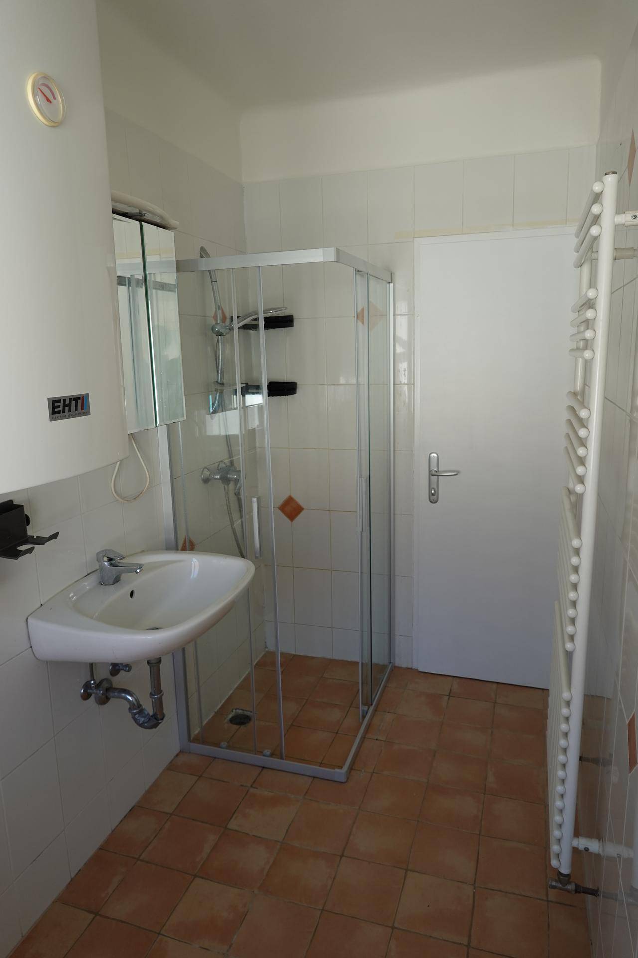 Badezimmer mit Duschkabine, Waschbecken und einem weißen Handtuchheizkörper an der Wand.