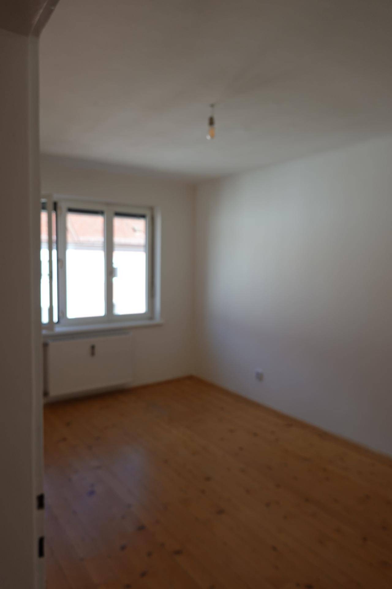 Unscharfer Innenraum mit Holzboden und einem Fenster, das Tageslicht hereinlässt.