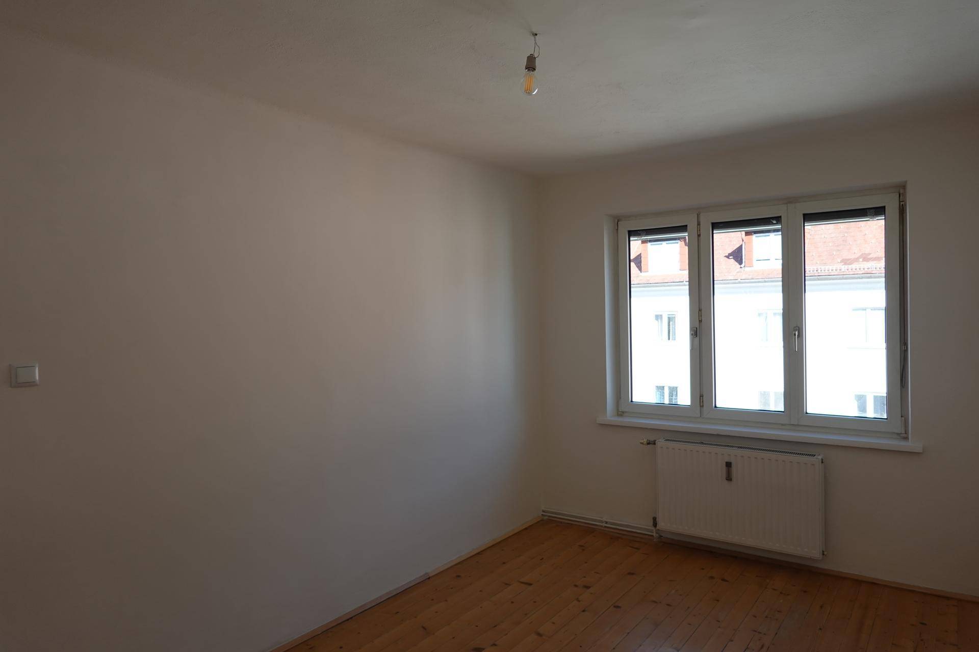 Heller Raum mit Holzboden, großem Fenster und einem Heizkörper unter dem Fenster.