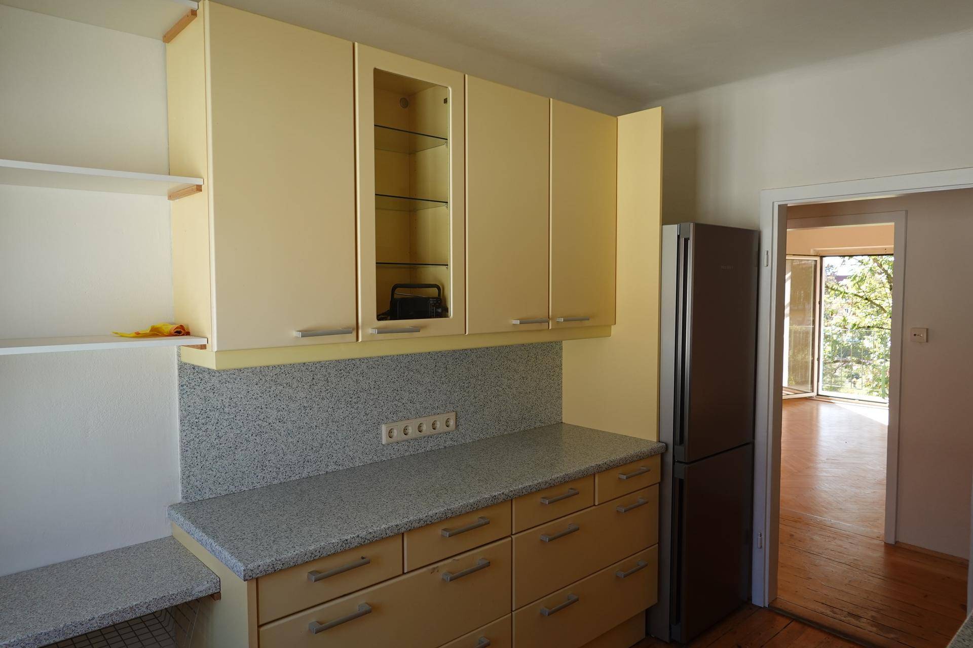 Küche mit gelben Ober- und Unterschränken, Arbeitsplatte und einem freistehenden Kühlschrank.