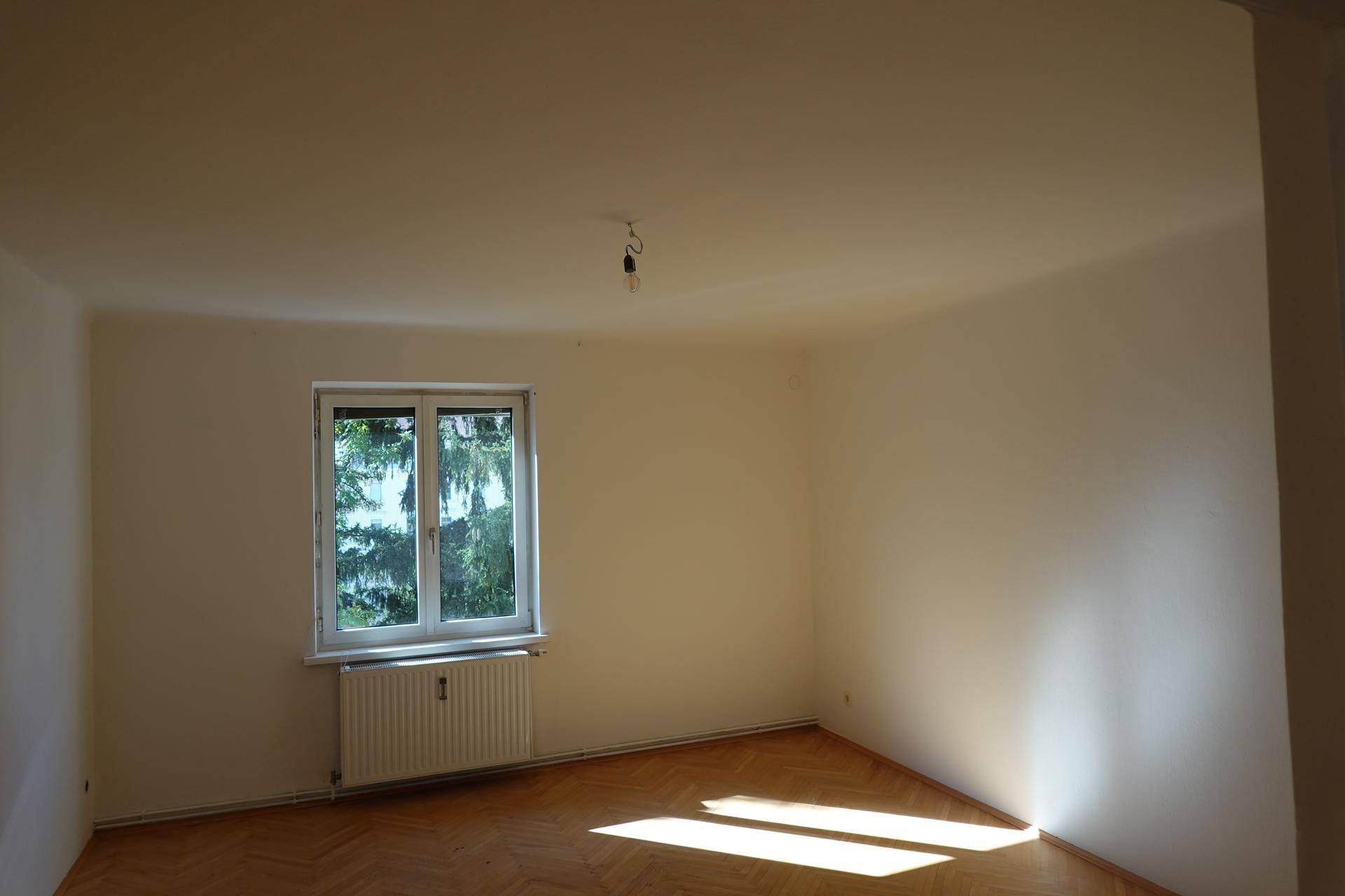 Sonniger Raum mit Fischgrätparkett, Fenster und Blick ins Grüne, ideal für Entspannung.