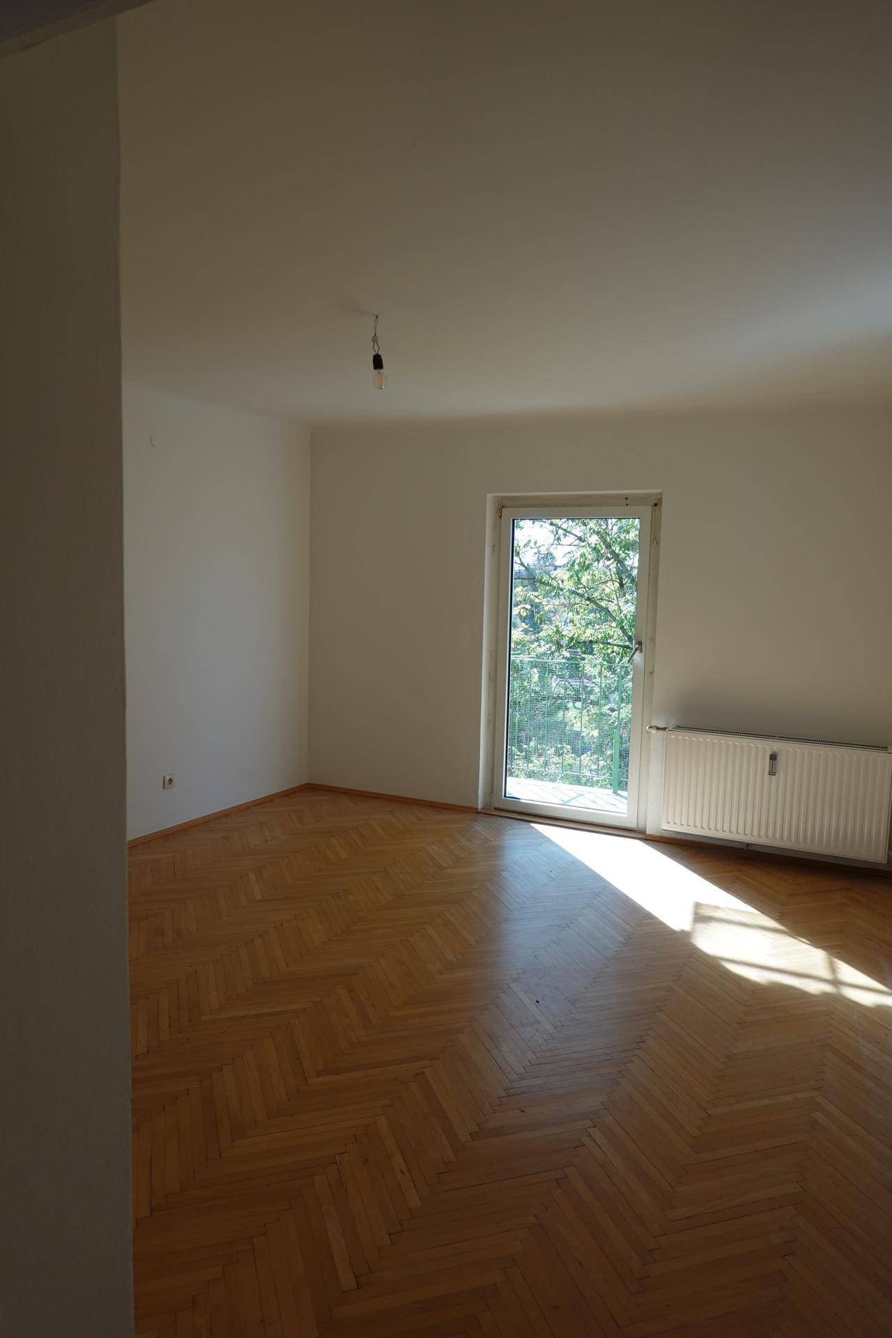 Heller Raum mit Fischgrätparkett und einer Tür, die zu einem Balkon oder Garten führt.