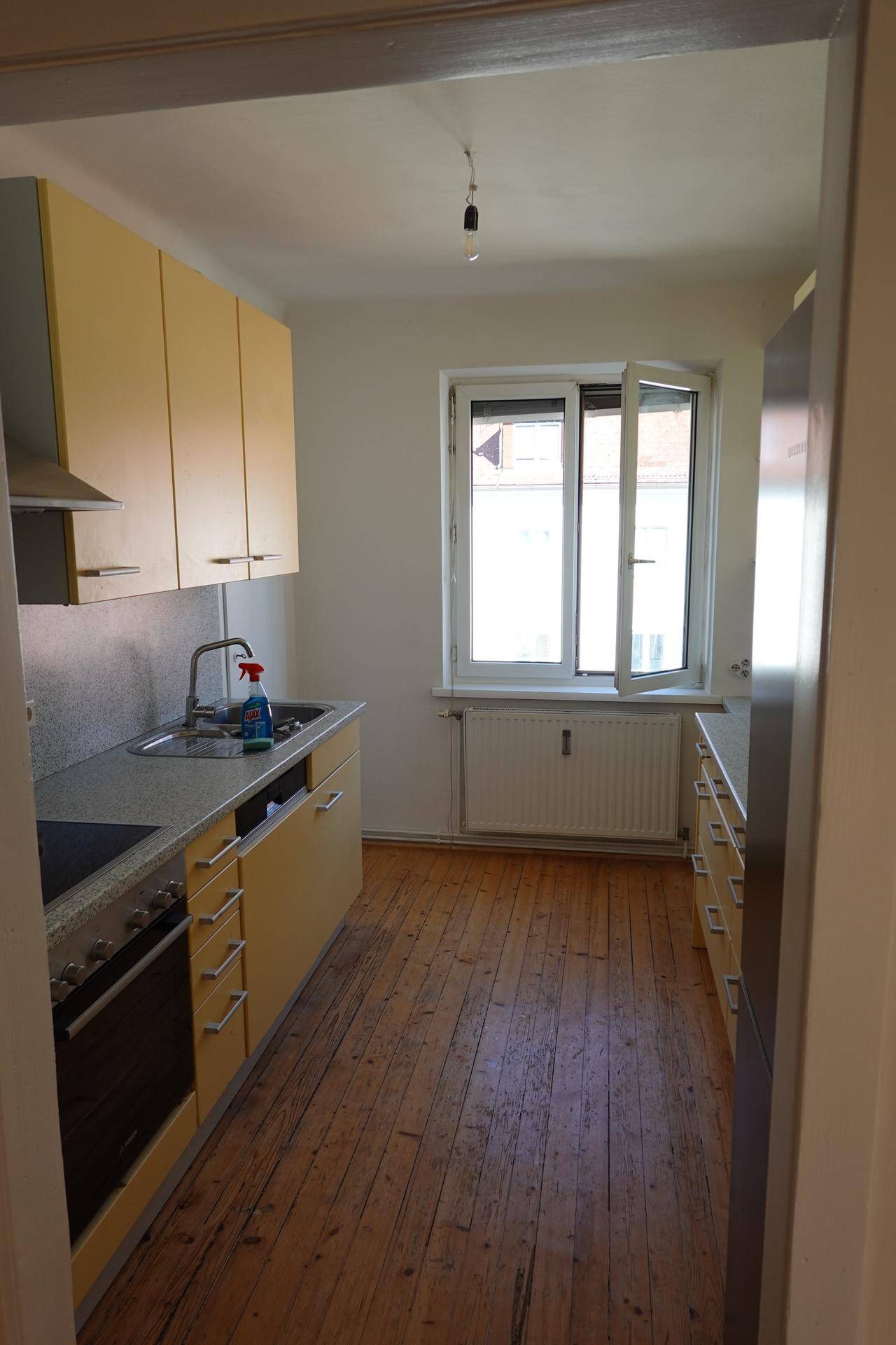 Helle Küche mit gelben Schränken, Holzdielenboden und einem Fenster mit Heizkörper.