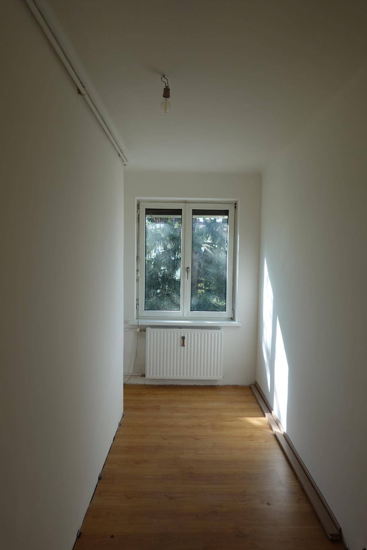 Schmaler Flur mit Holzboden, Fenster und viel Tageslicht, das den Raum erhellt.