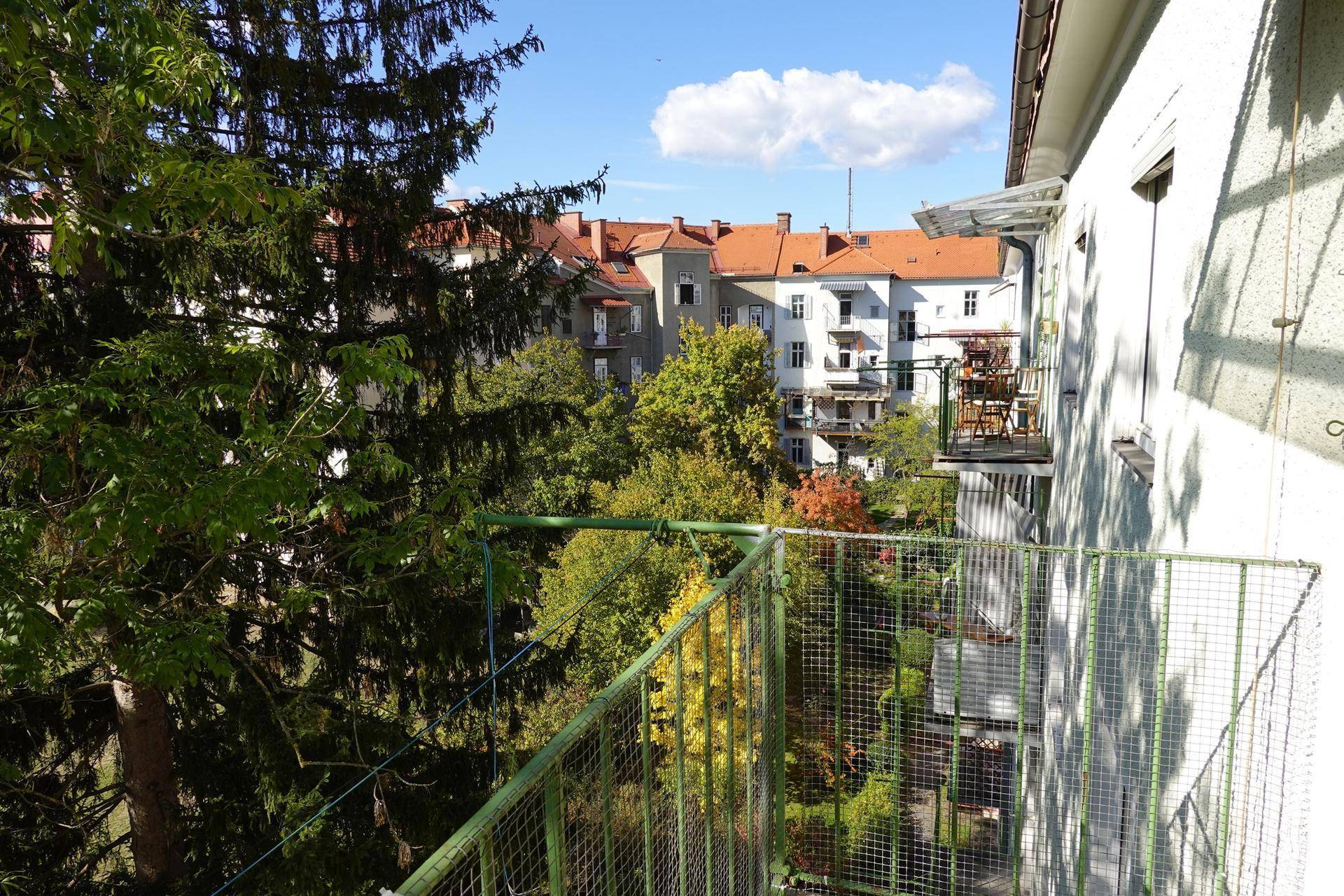 Balkon mit grüner Gitterumzäunung und weitem Blick auf Bäume und Wohngebäude.