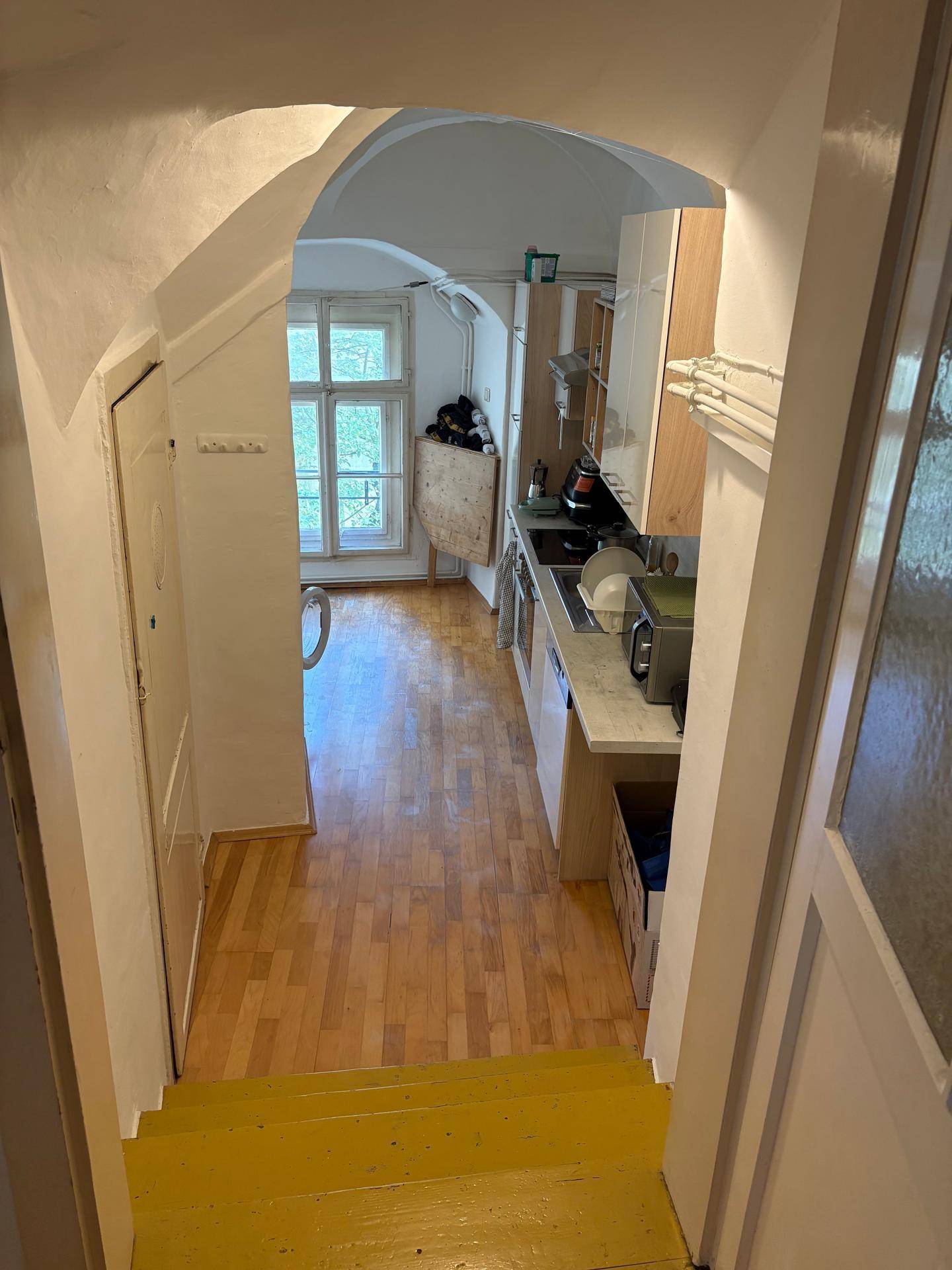 Blick von der Treppe in eine schmale Küche mit Holzboden und Fenster.