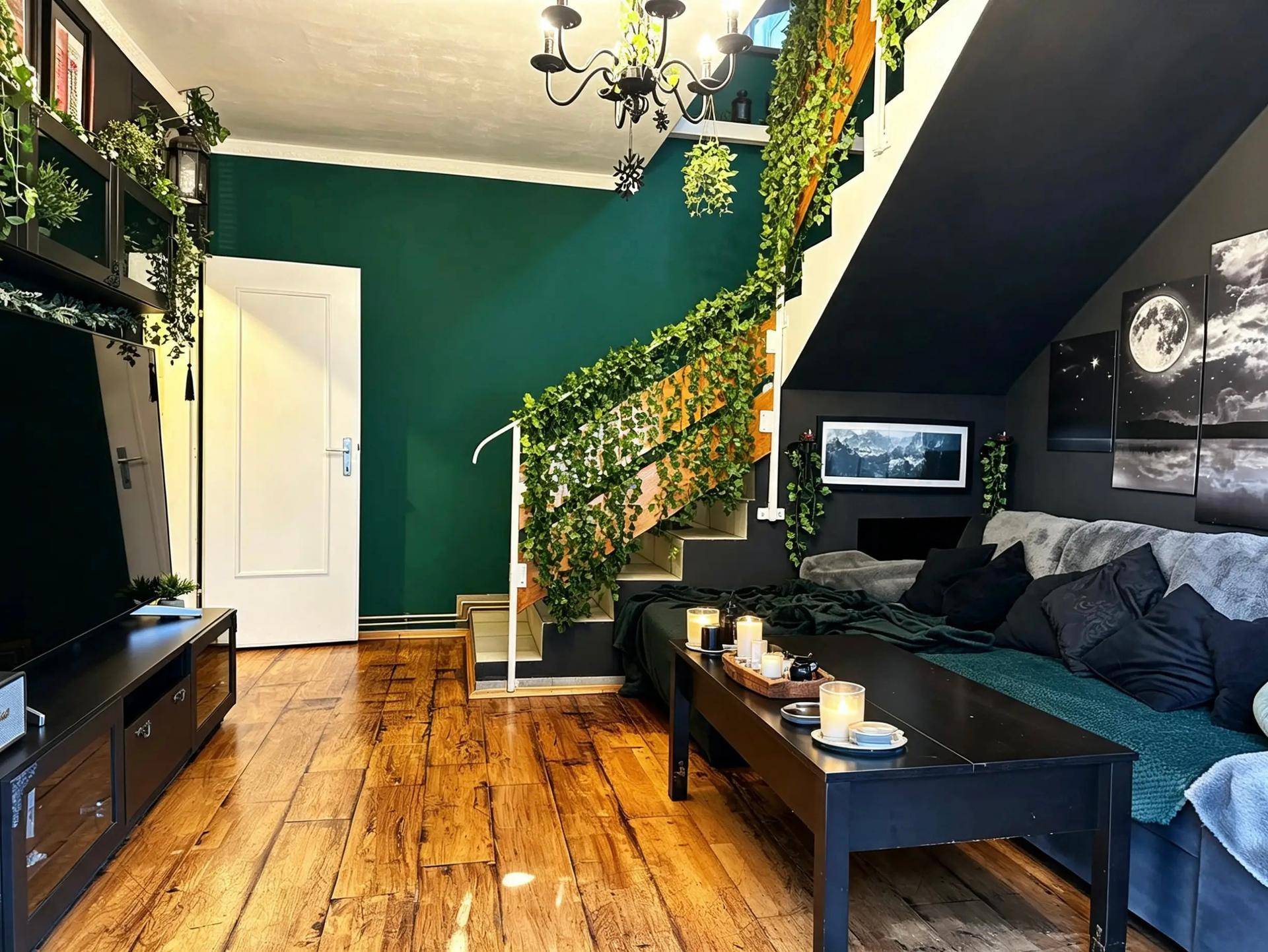 Dunkelgrünes Wohnzimmer mit Holzboden, gemütlichem Sofa und einer mit Pflanzenranken verzierten Treppe.