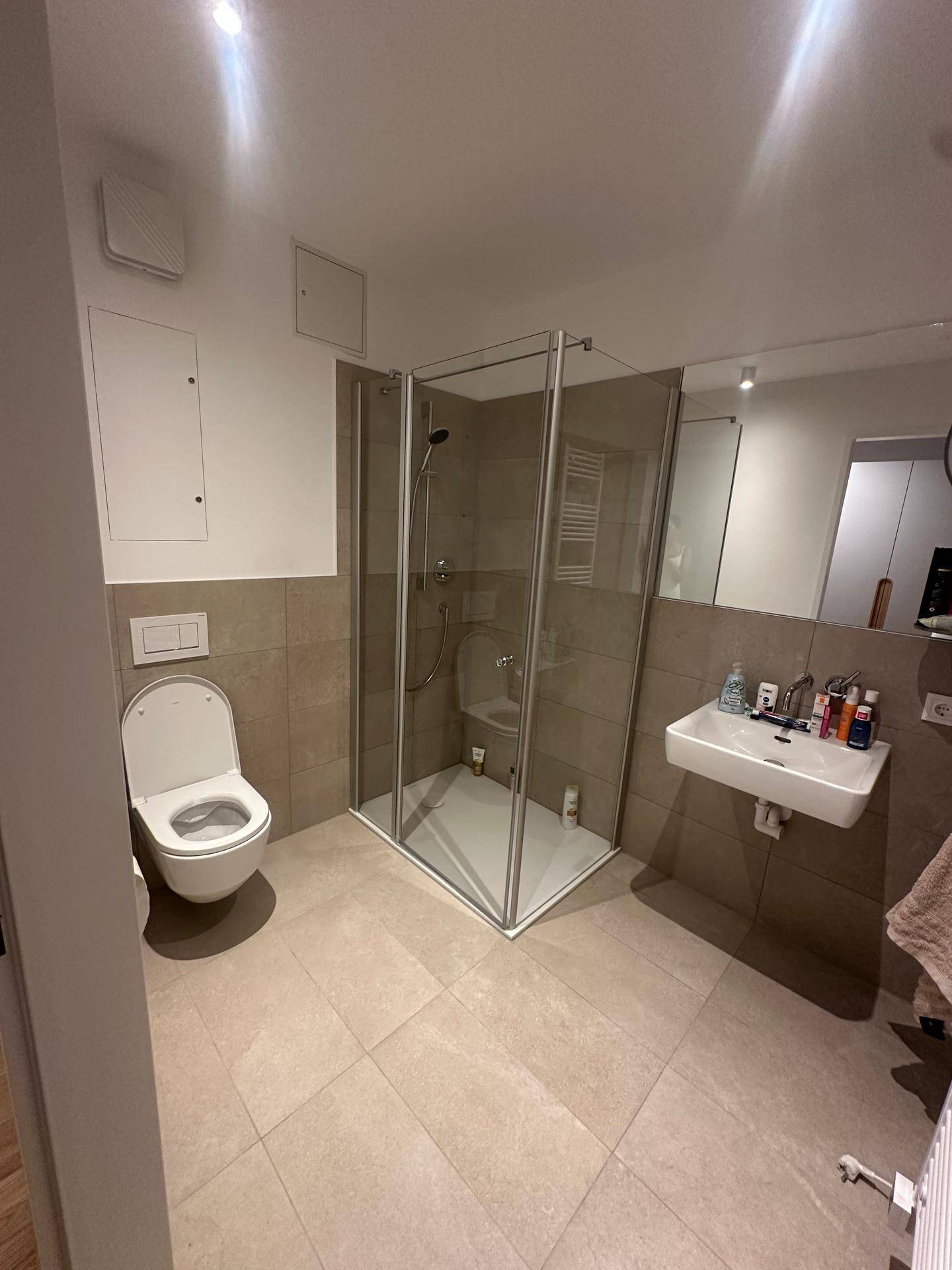 Helles Badezimmer mit Duschkabine, wandhängendem WC und modernem Waschbecken auf beigefarbenen Fliesen.