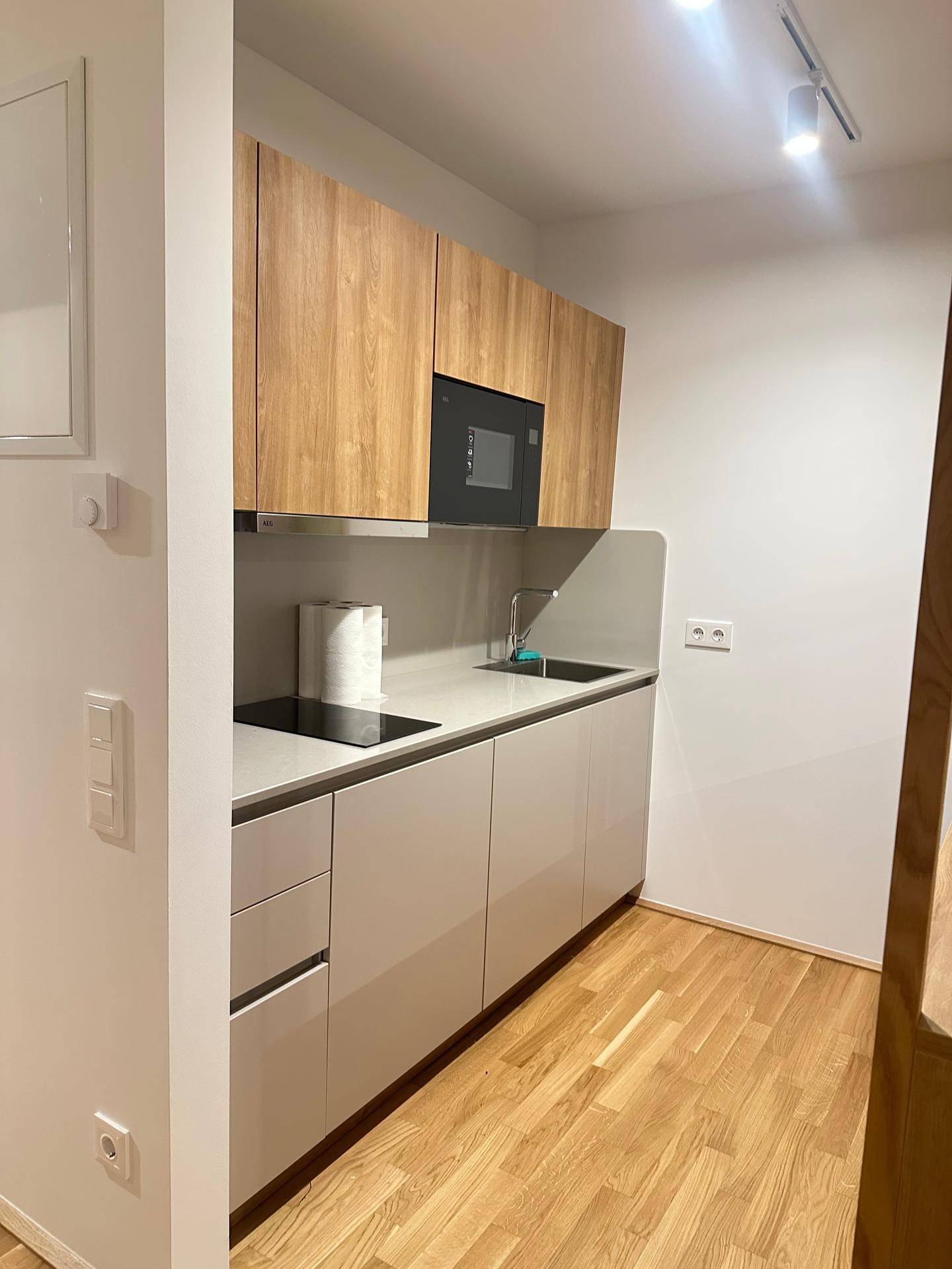 Kompakte Küchenzeile mit Holzschränken, Induktionskochfeld, Spüle und integrierter Mikrowelle.
