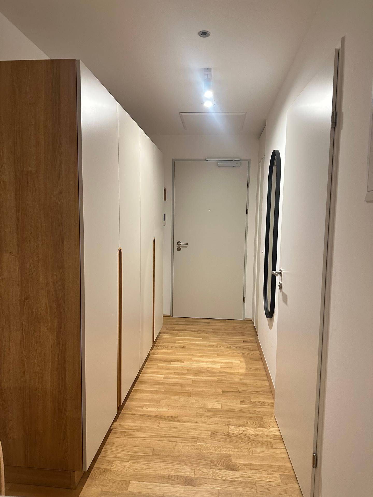 Heller Flur mit Einbauschränken und Holzfußboden, der zu den weiteren Räumen führt.