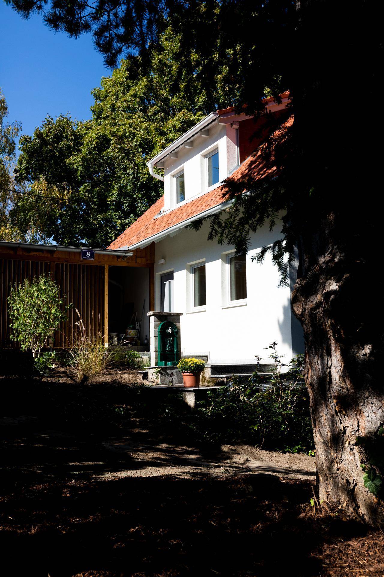 Weißes Wohnhaus mit rotem Ziegeldach, umgeben von üppigem Grün und Bäumen.