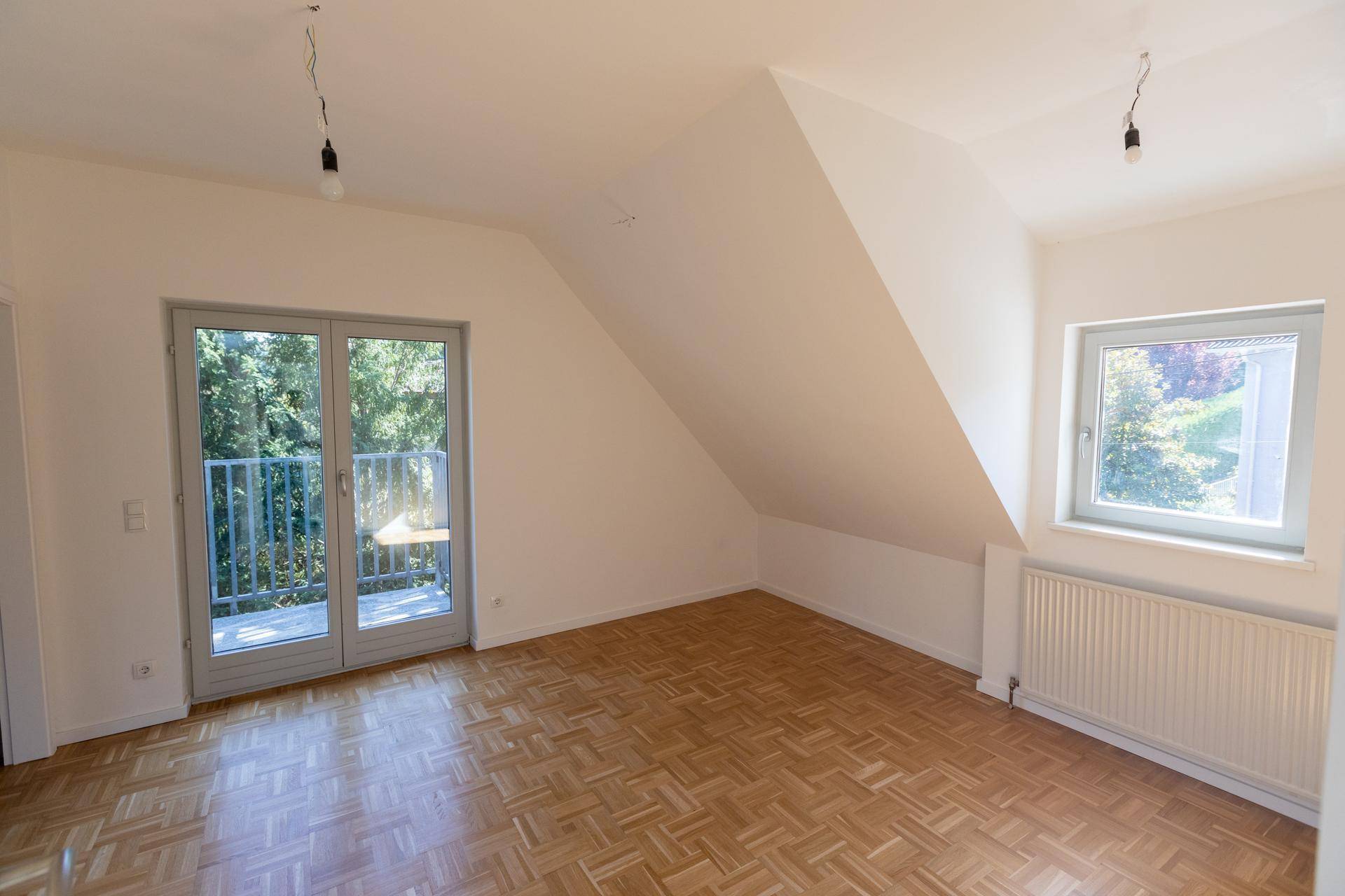 Helles Schlafzimmer im Dachgeschoss mit schrägen Wänden, Parkettboden und Balkonzugang.