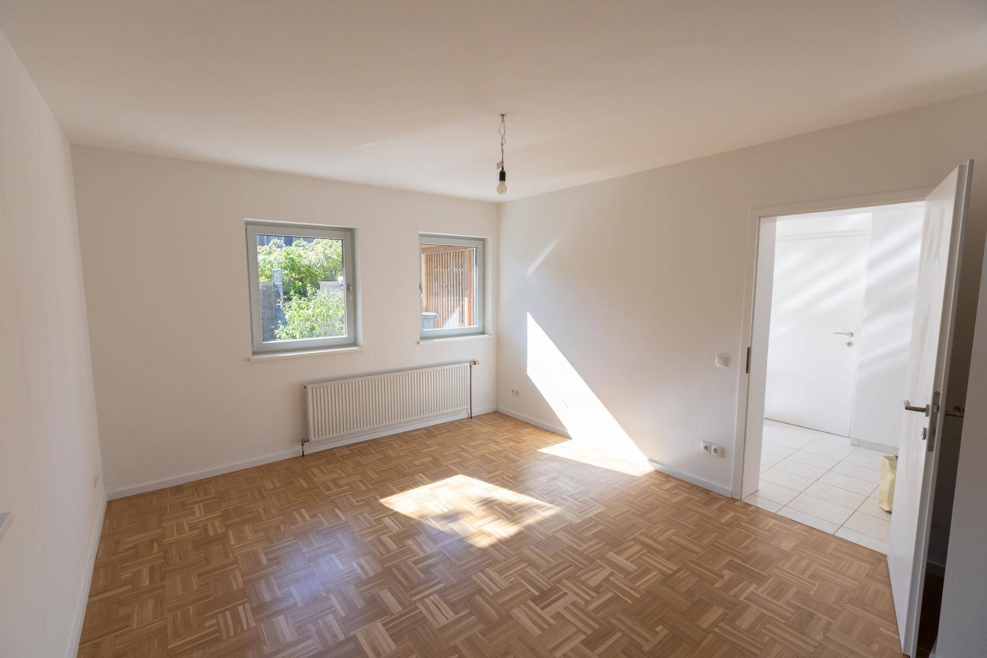 Heller Raum mit Parkettboden und Fenstern, die viel natürliches Sonnenlicht hereinlassen.