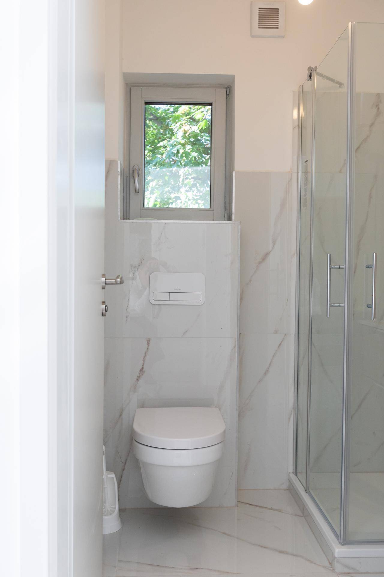 Helles Badezimmer mit wandhängendem WC, Fenster und modernen Marmor-Effekt-Fliesen.