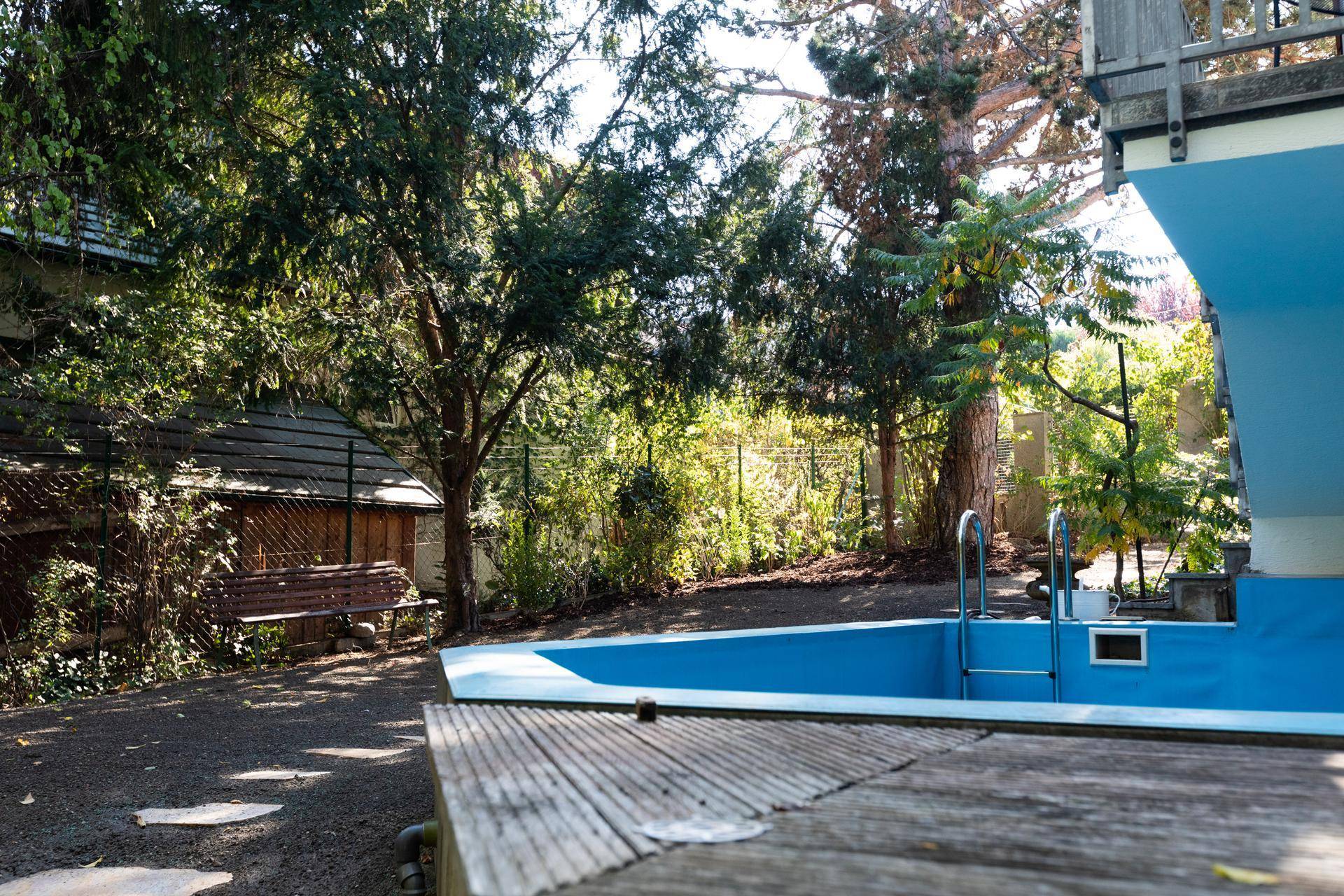 Kleiner Poolbereich im Garten mit Holzdeck und umgebender grüner Bepflanzung.
