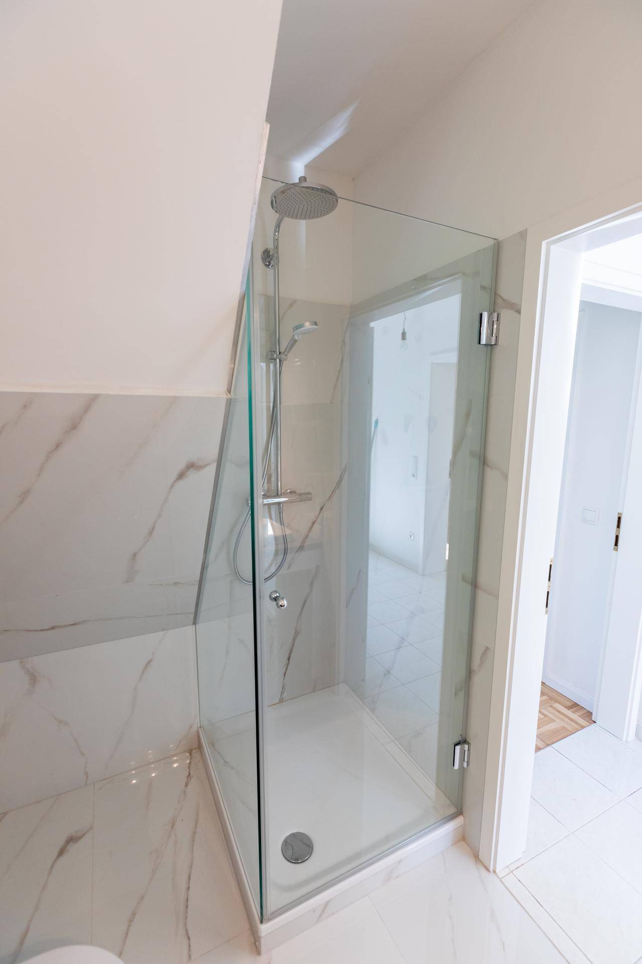 Modernes Badezimmer mit Duschkabine aus Glas, eleganten Marmorfliesen und Dachschräge.