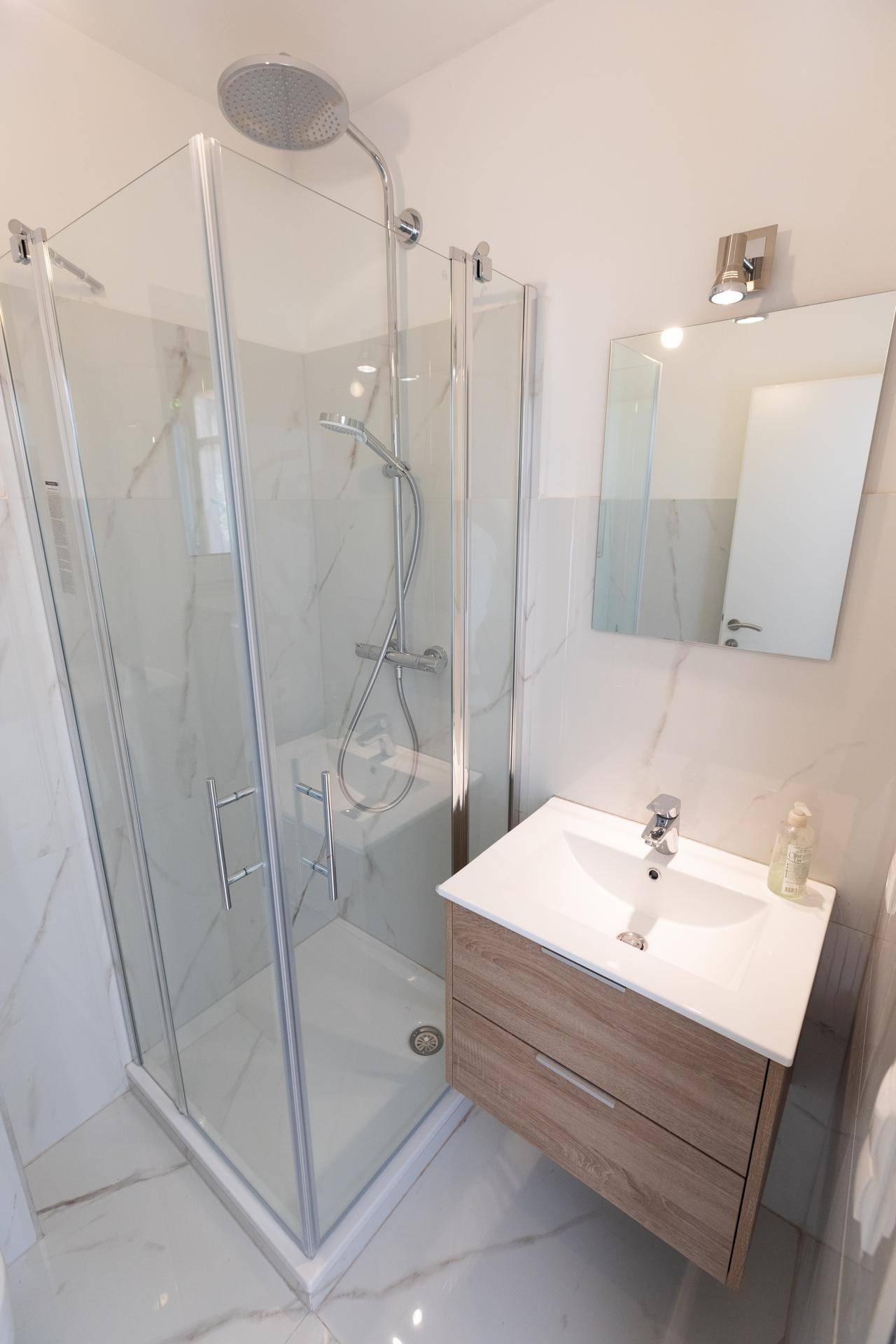 Modernes Badezimmer mit Duschkabine aus Glas, eleganten Marmorfliesen und einem Einzelwaschbecken.