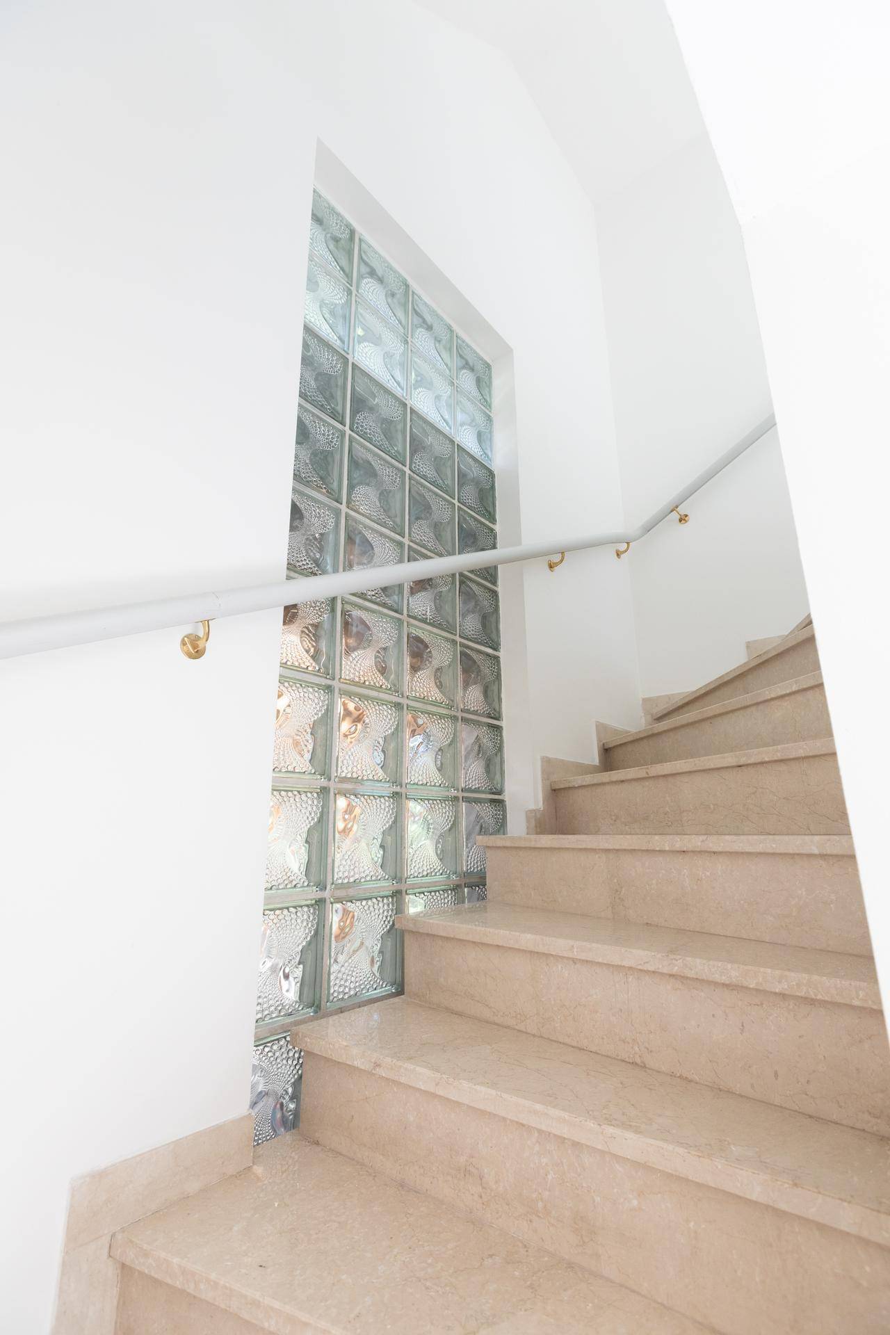 Elegantes Treppenhaus mit Natursteinstufen und einer Glasbausteinwand für helles Tageslicht.