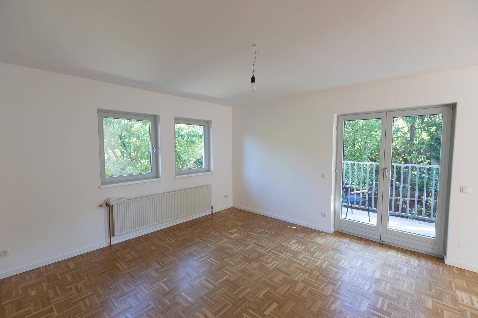 Geräumiges Wohnzimmer mit Parkettboden, großen Fenstern und direktem Zugang zum Außenbereich.
