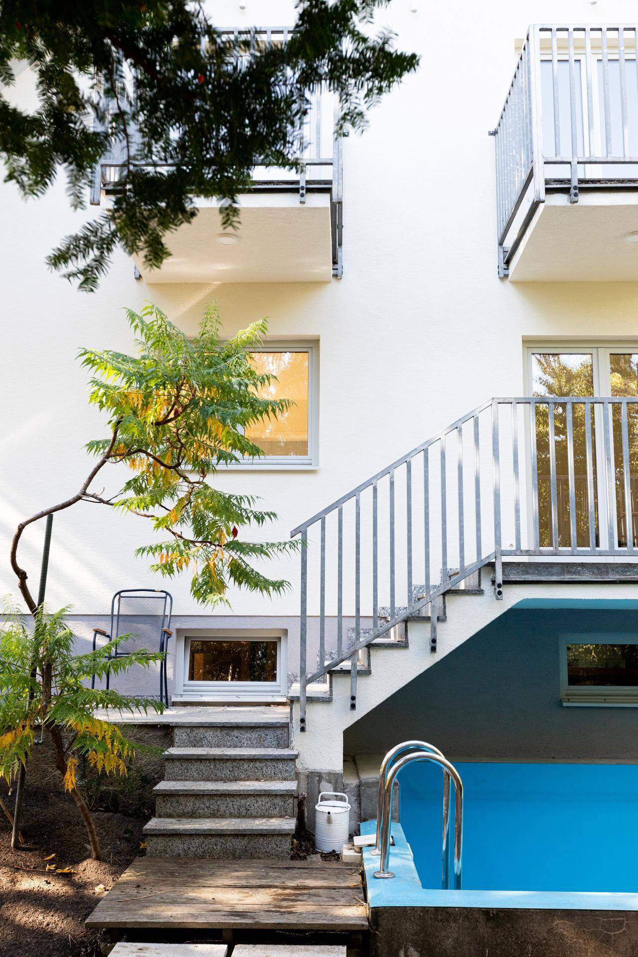 Außenansicht des Gebäudes mit Treppe, Balkonen und einem kleinen Pool im Gartenbereich.