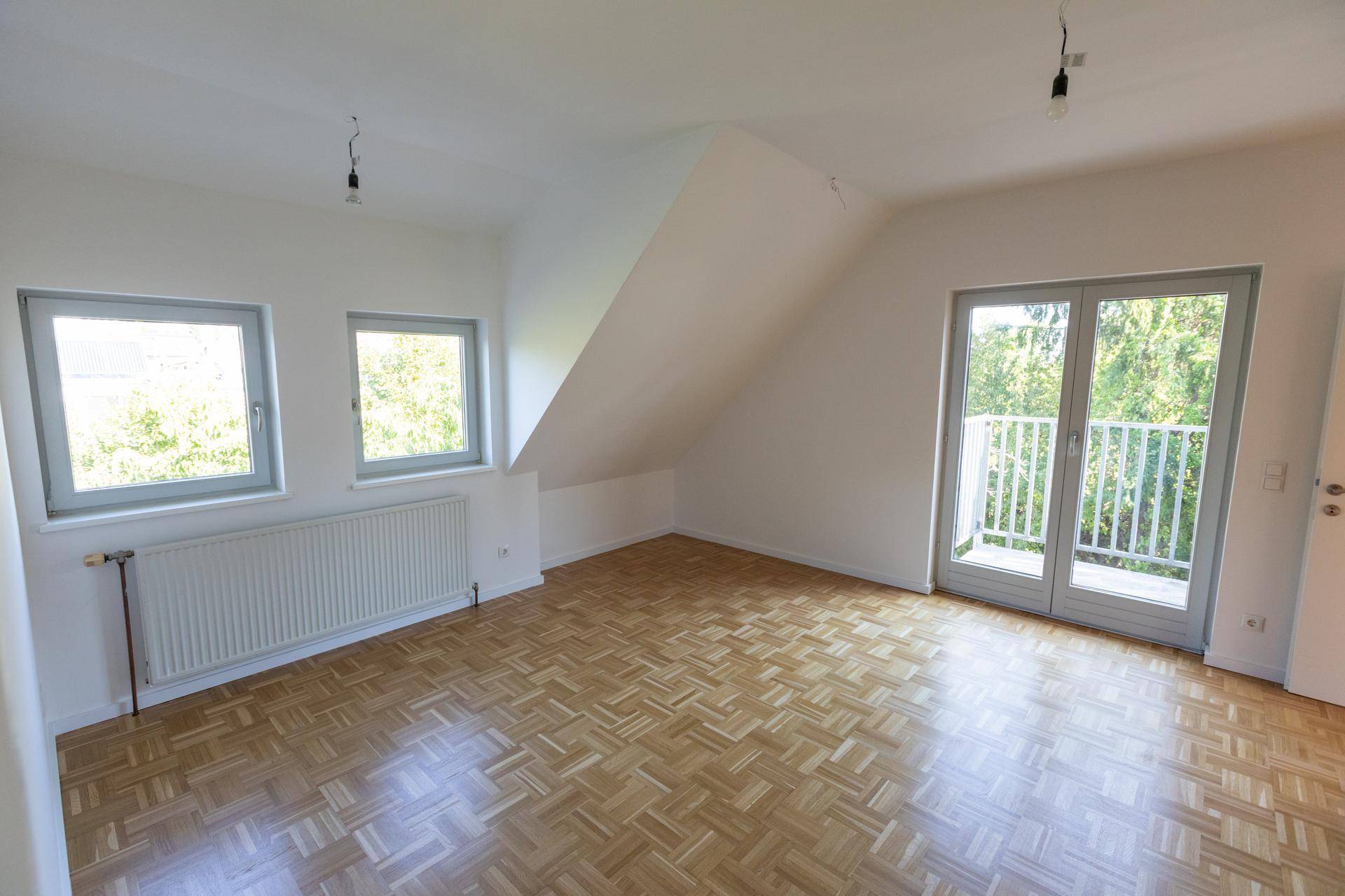 Lichtdurchflutetes Dachgeschoss-Schlafzimmer mit Parkettboden, zwei Fenstern und Balkonzugang.