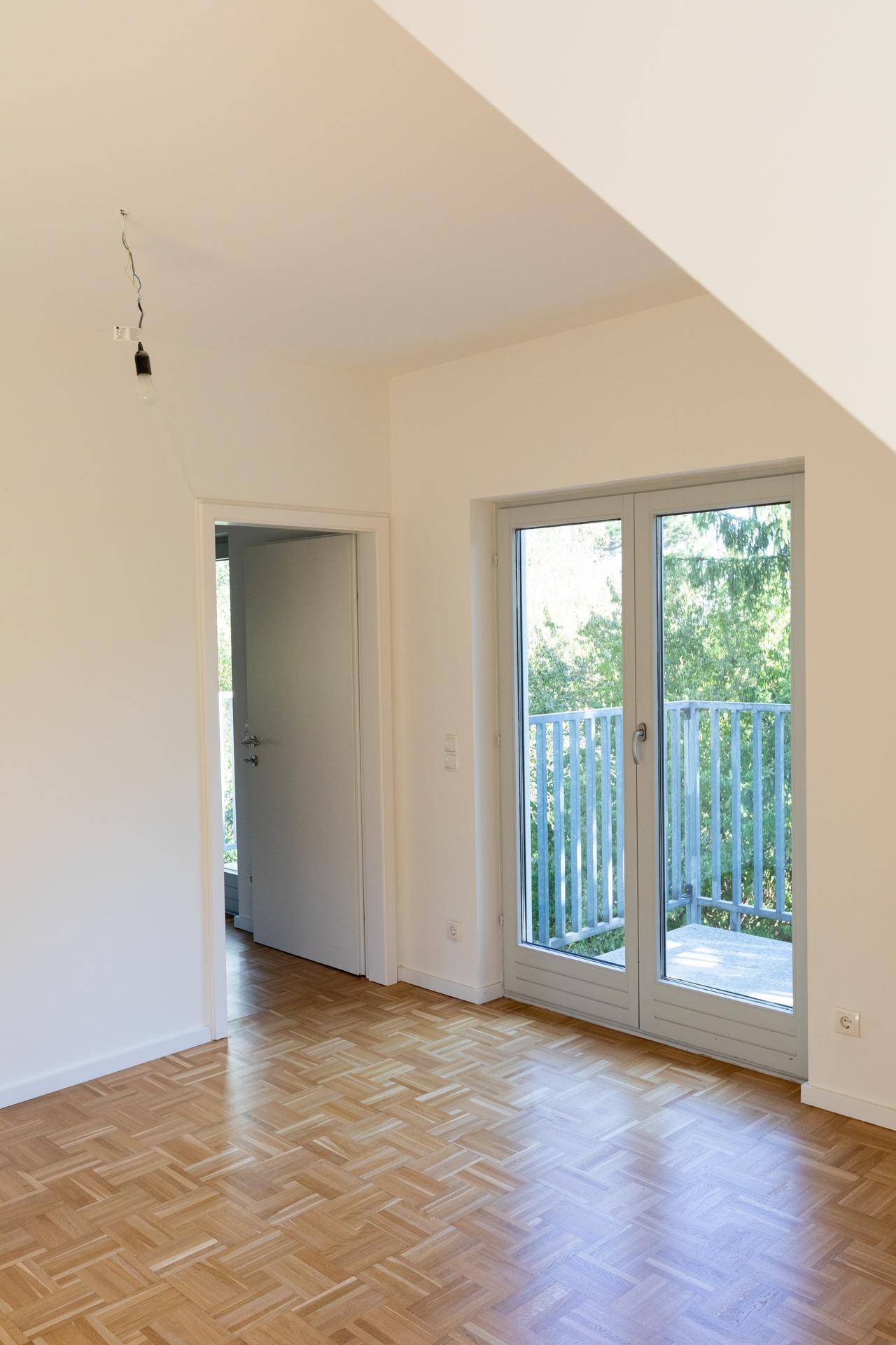 Geräumiges Schlafzimmer im Dachgeschoss mit Parkettboden und direktem Zugang zu einem Balkon.