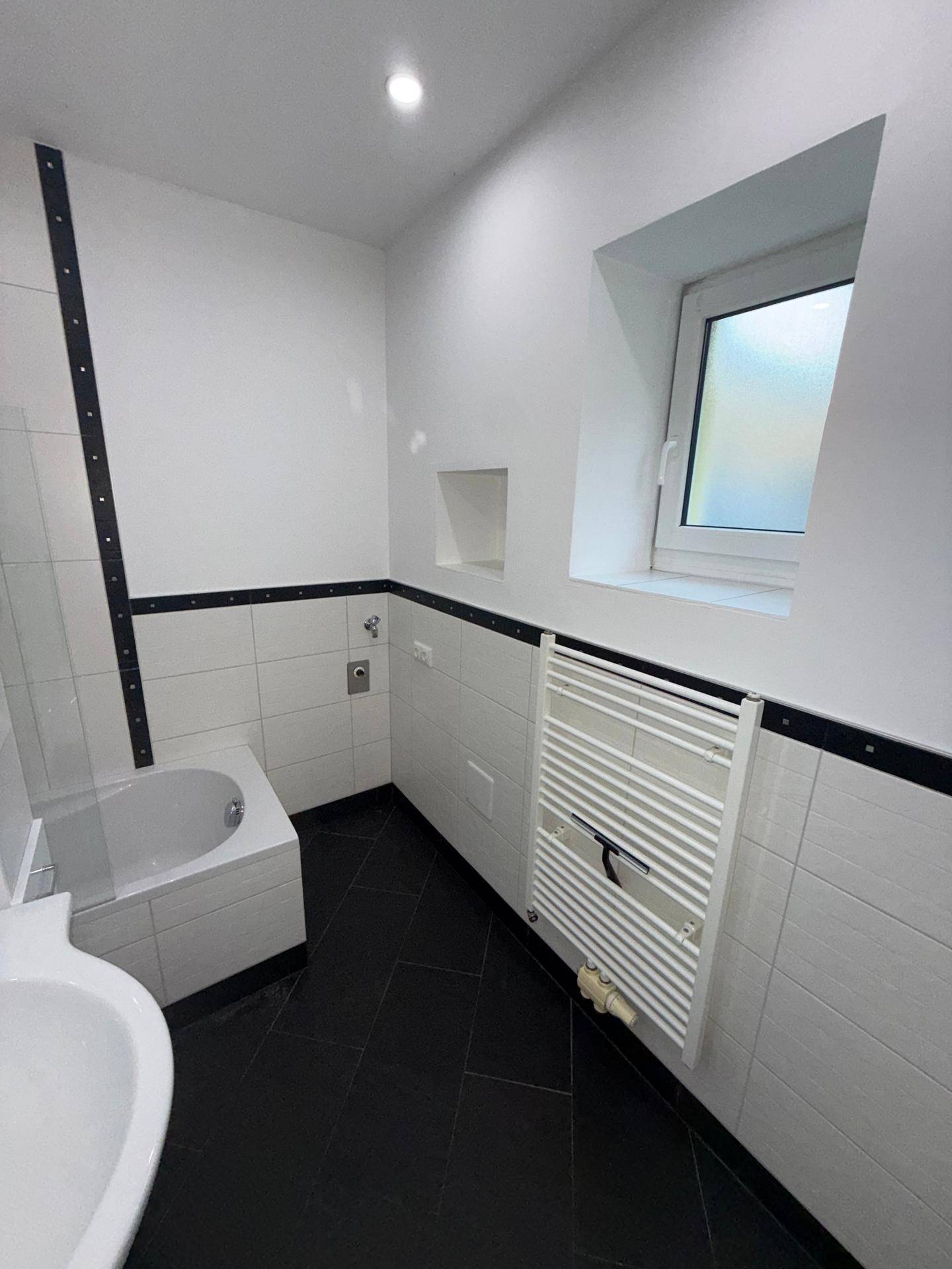 Badezimmer mit Badewanne, beheiztem Handtuchhalter und einem Fenster für Tageslicht.