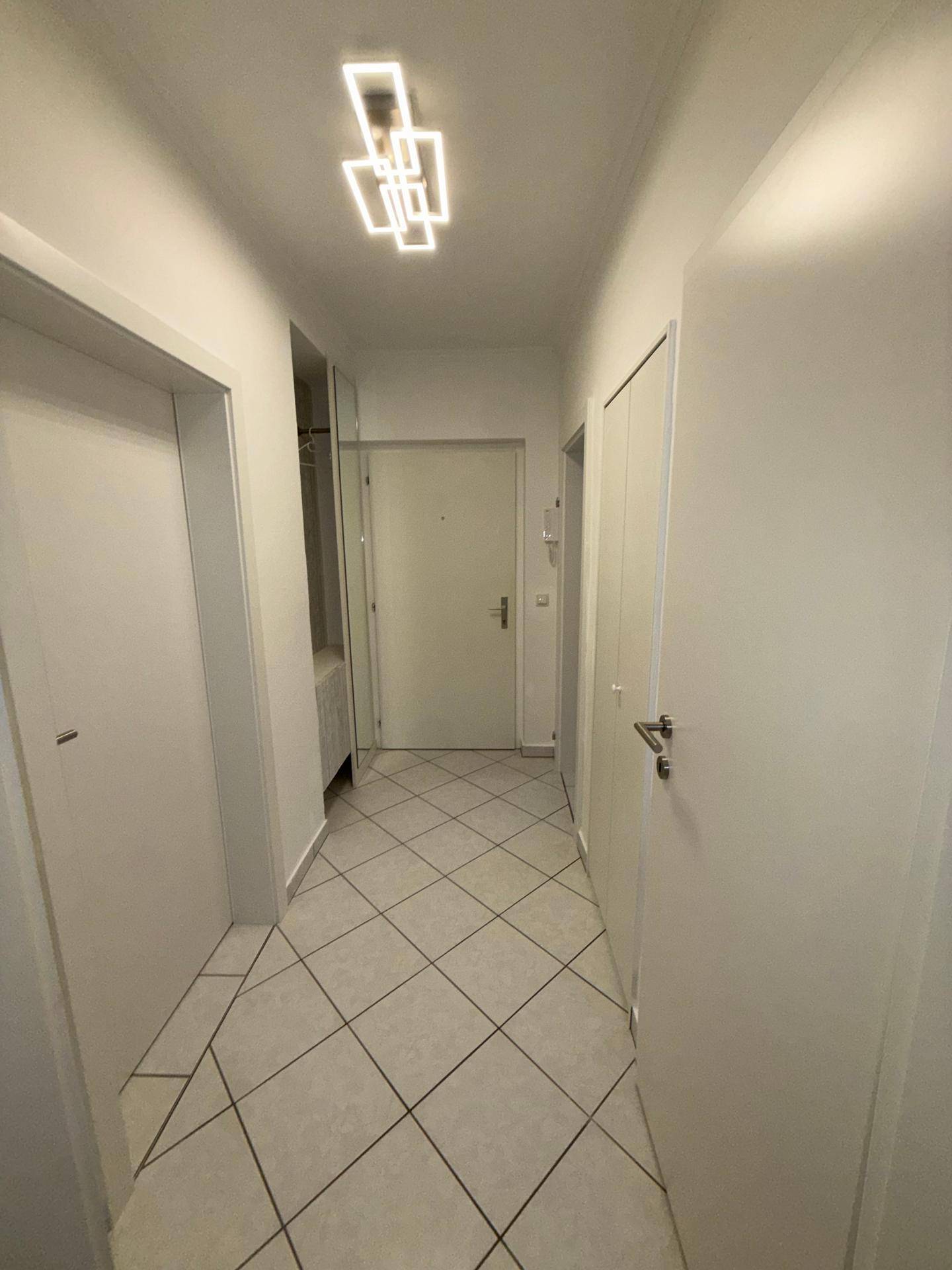 Langer Flur mit hellen Fliesen, weißen Türen und integrierten Schränken für Stauraum.