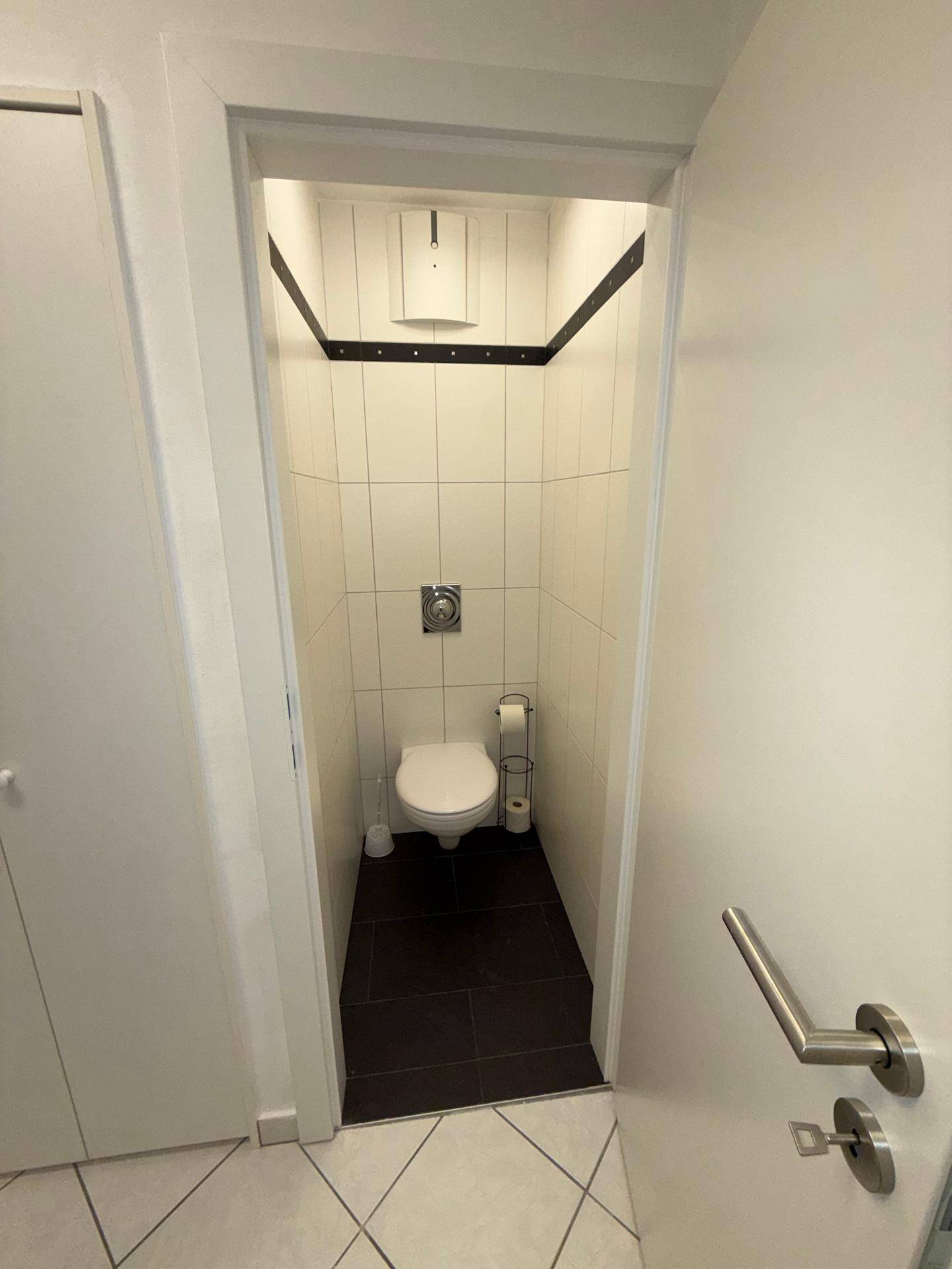 Kleines Gäste-WC mit weißen Wandfliesen, dunklem Boden und wandhängendem WC.