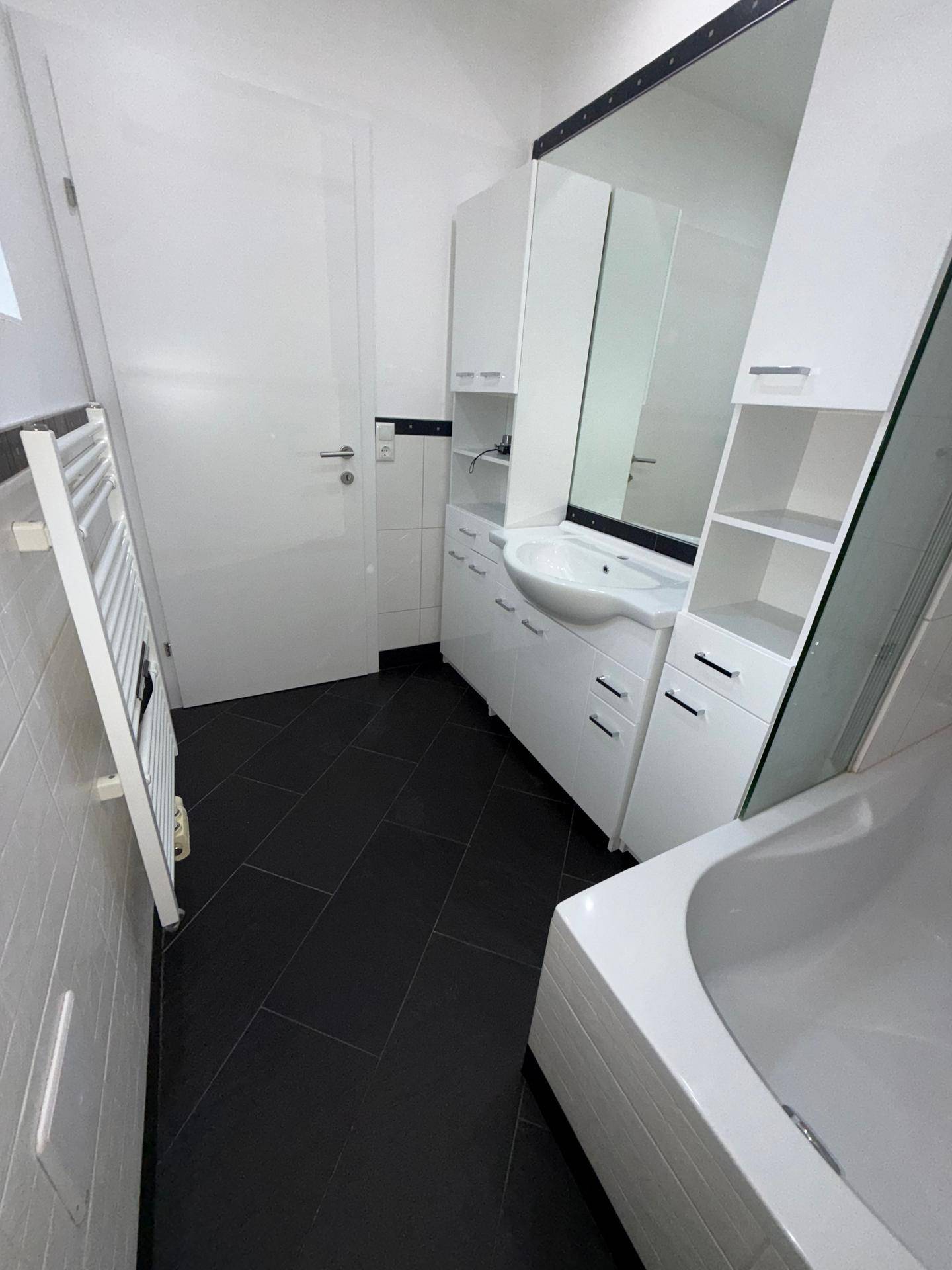 Helles Badezimmer mit dunklem Fliesenboden, Waschtisch, Badewanne und beheiztem Handtuchhalter.