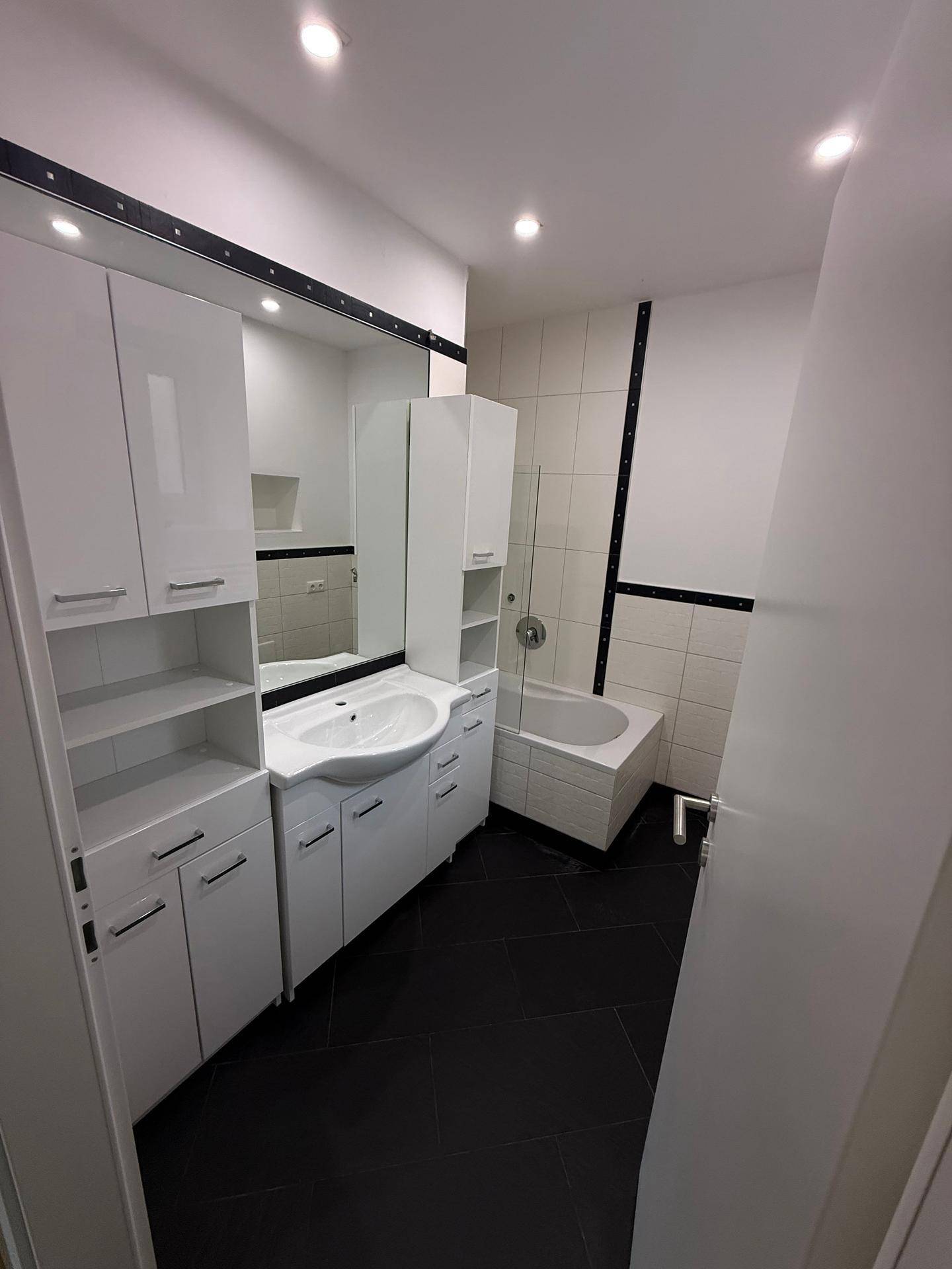 Modernes Badezimmer mit dunklem Fliesenboden, weißem Waschtisch und Badewanne.