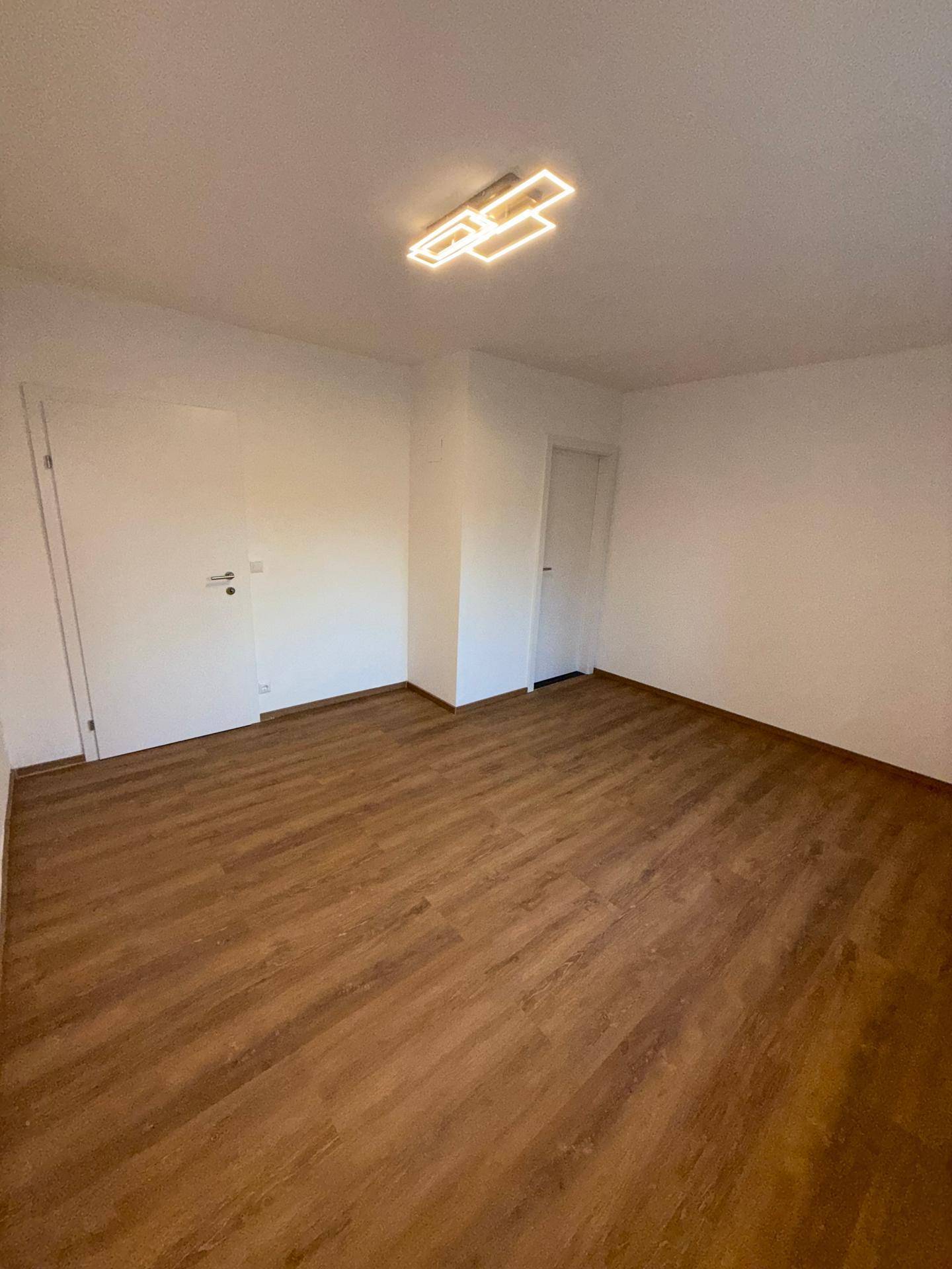 Geräumiges Zimmer mit hellem Laminatboden und zwei weißen Türen, bereit zur individuellen Gestaltung.