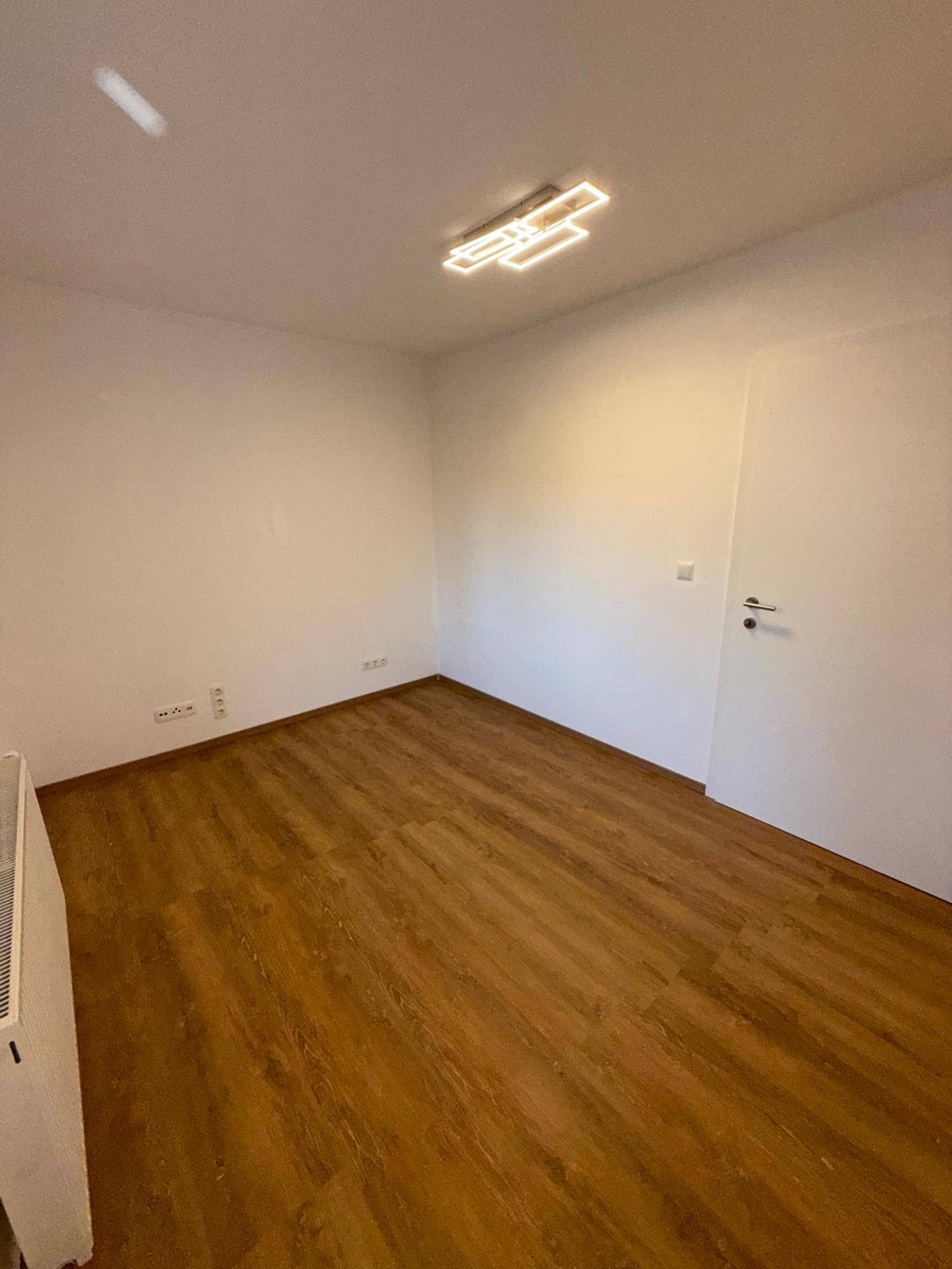 Leeres Zimmer mit Laminatboden, weißen Wänden und einem Heizkörper, ideal für ein Schlafzimmer.