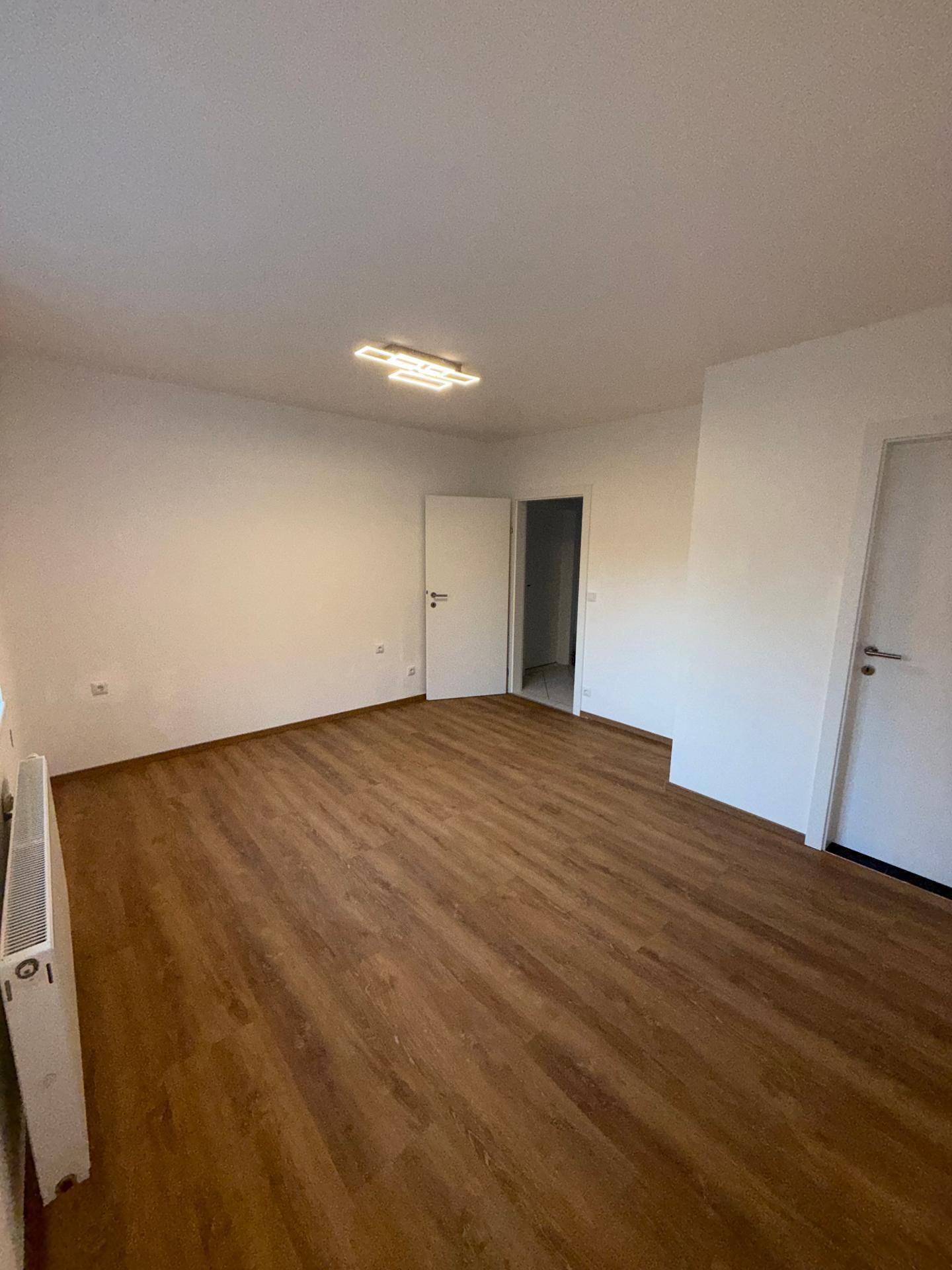 Helles Zimmer mit Laminatboden und offenen Türen, die zu weiteren Bereichen der Wohnung führen.