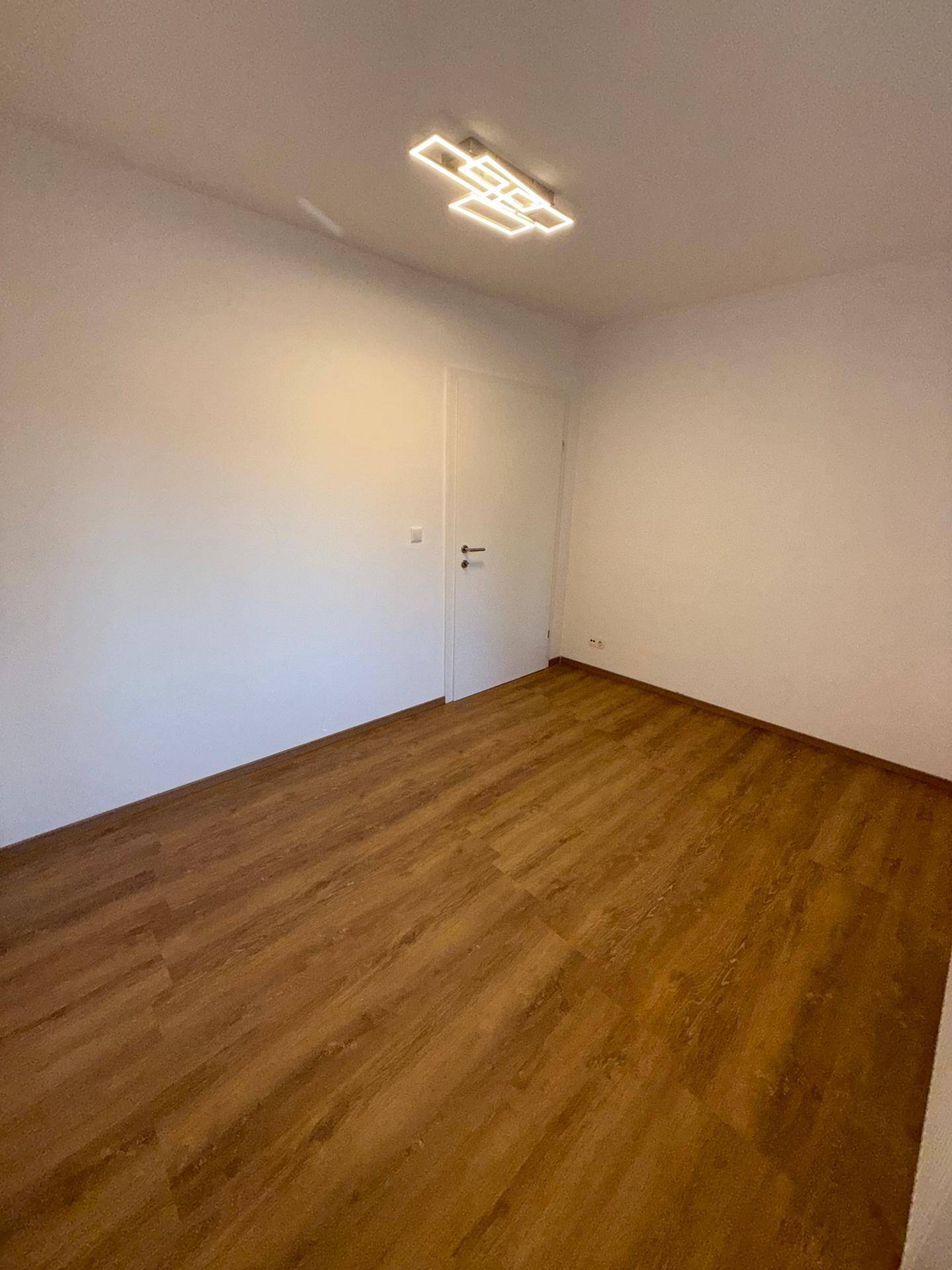 Schlichtes Zimmer mit neuem Laminatboden und weißen Wänden, bereit für die Einrichtung.