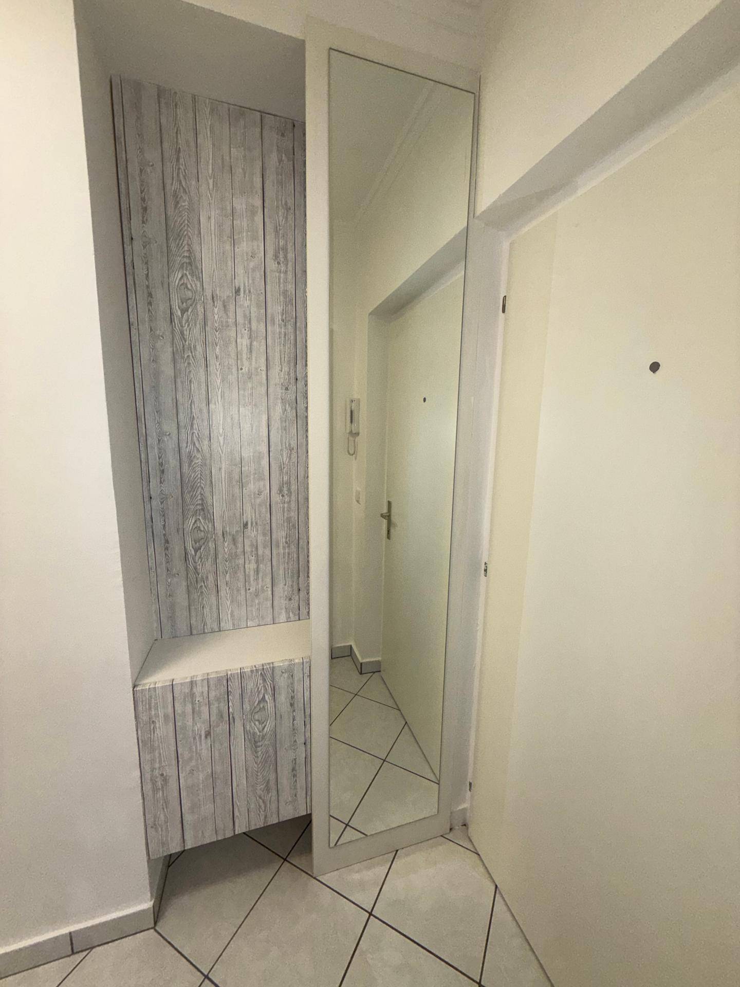 Detailansicht des Flurs mit einer Garderobennische in Holzoptik und einem großen Wandspiegel.
