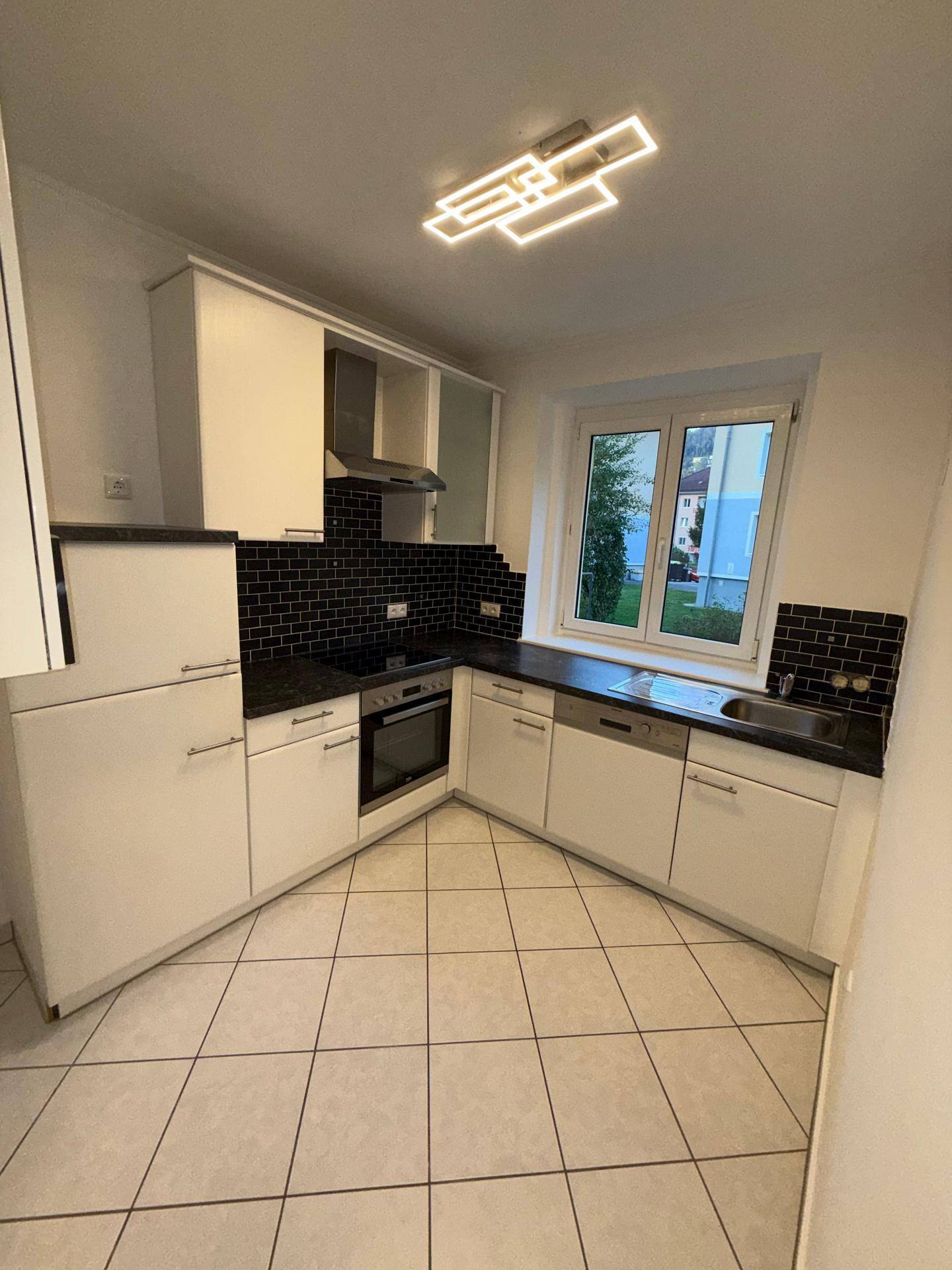 Moderne Küche mit weißen Einbauschränken, schwarzer Arbeitsplatte und Fenster mit Ausblick.