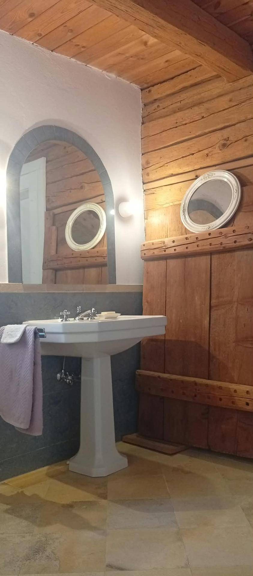 Badezimmer mit Standwaschbecken, großem Bogenspiegel und rustikalen Holzvertäfelungen an den Wänden.